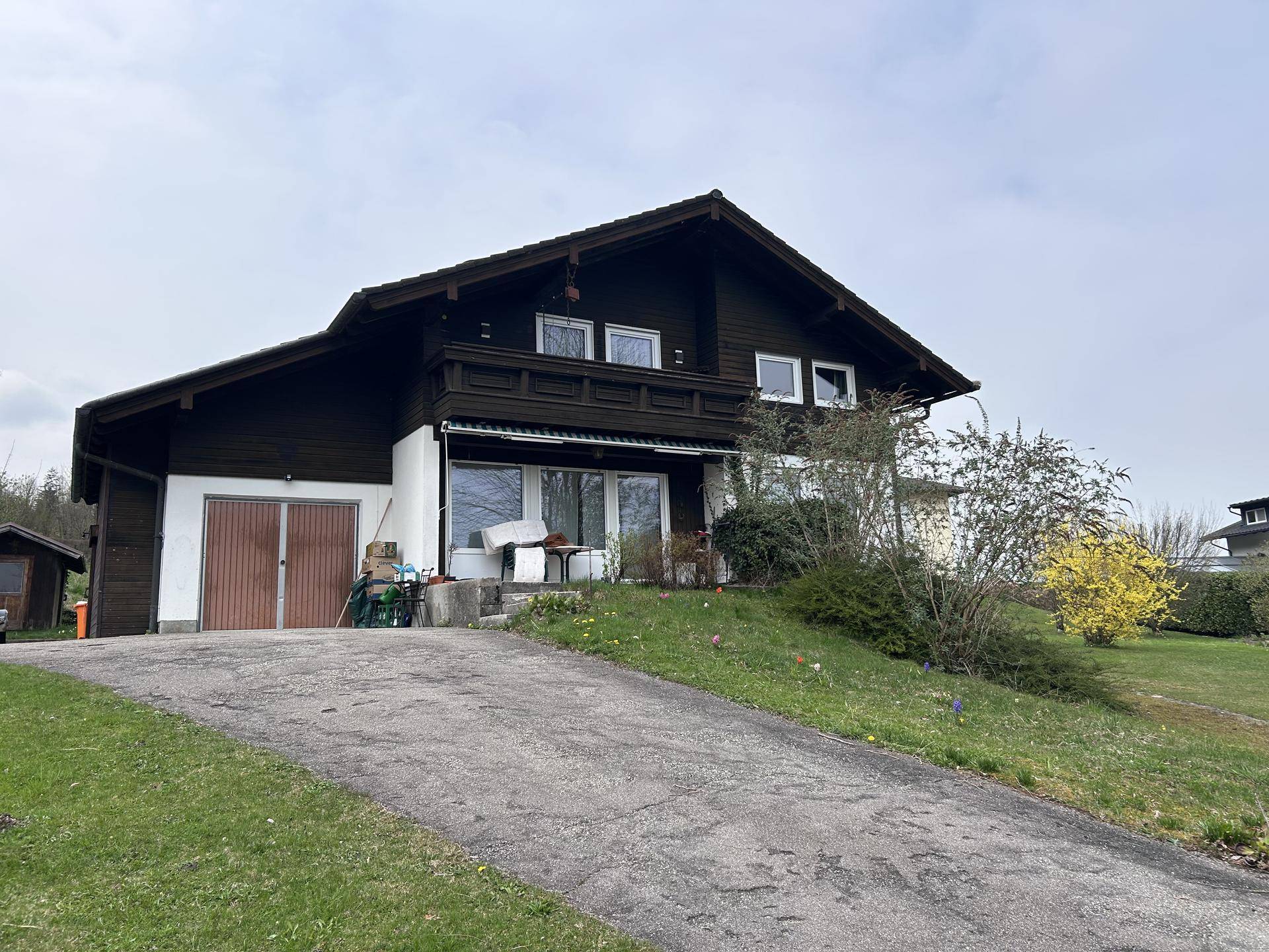 Traditionelles Holzhaus mit Satteldach und Auffahrt, umgeben von grüner Wiese und Bäumen.