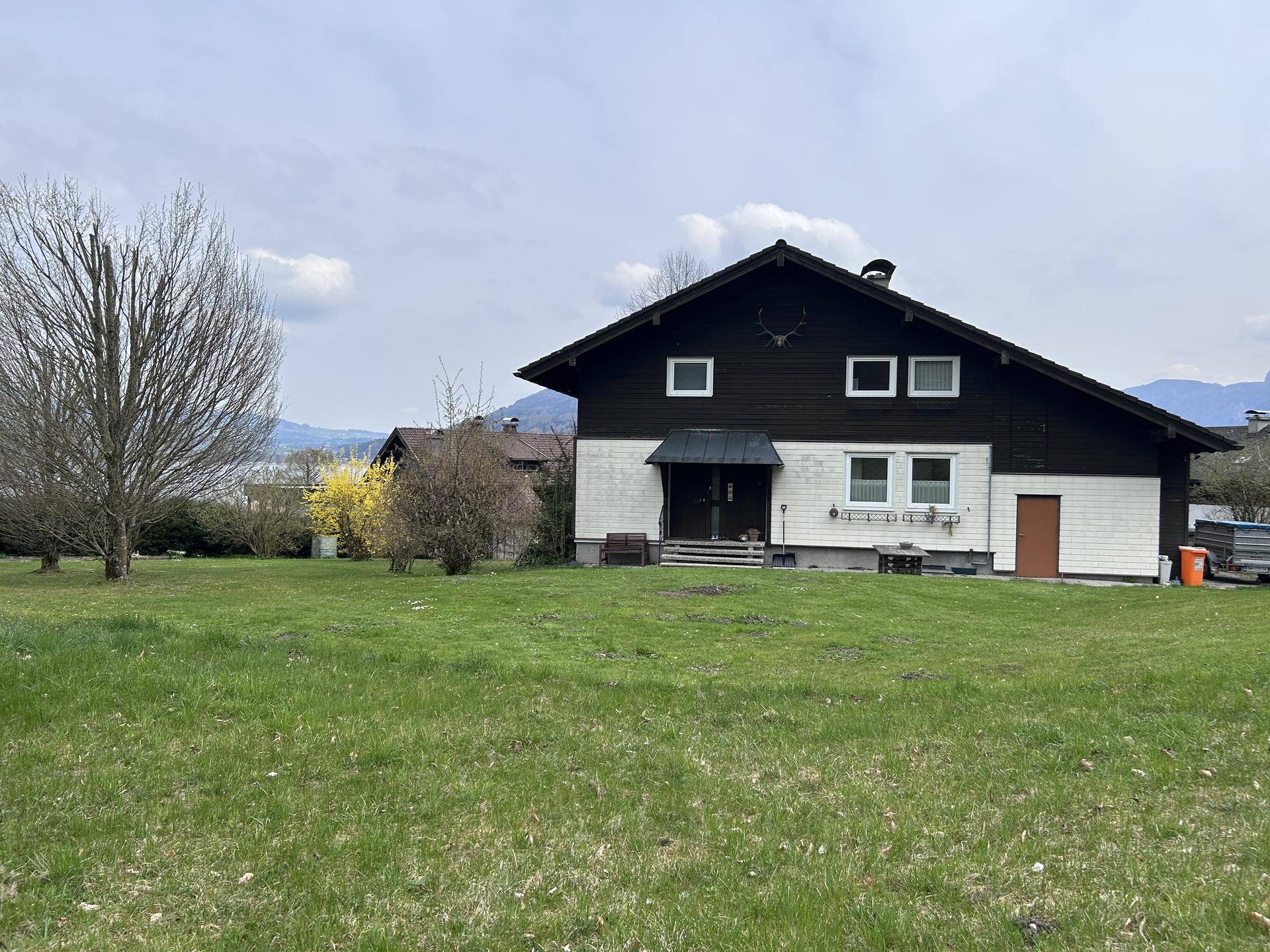 Rückansicht eines Holzhauses mit großem Garten und Blick auf die umliegende Landschaft.