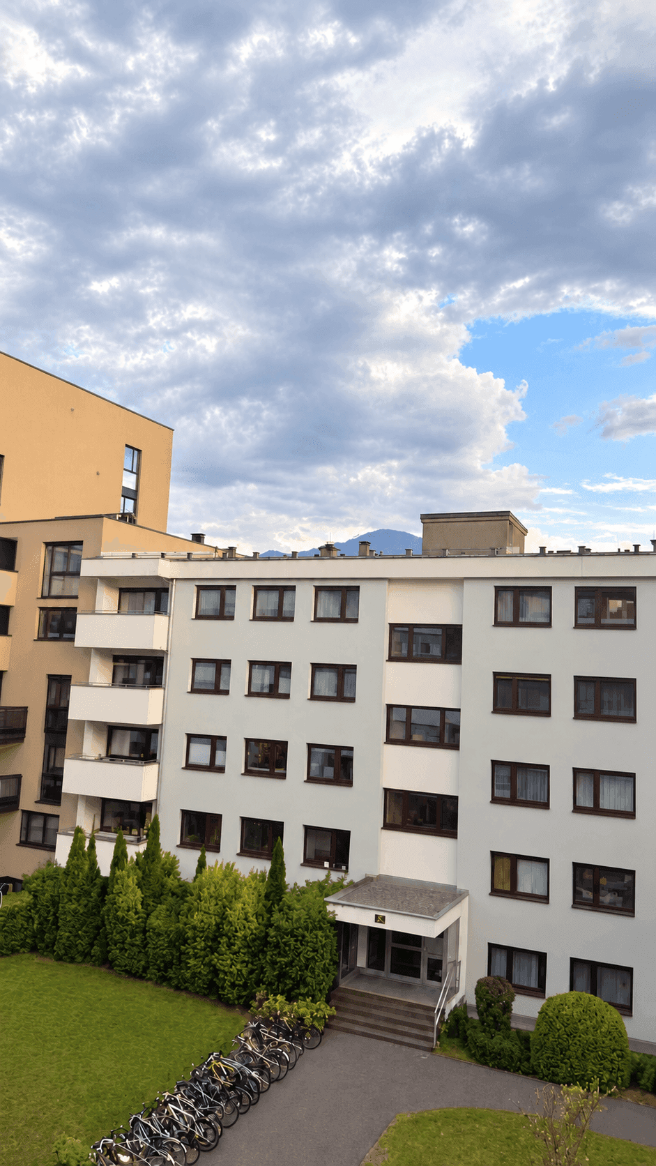 Mehrfamilienhaus mit Balkonen, gepflegter Grünfläche und Fahrradstellplätzen im Freien.