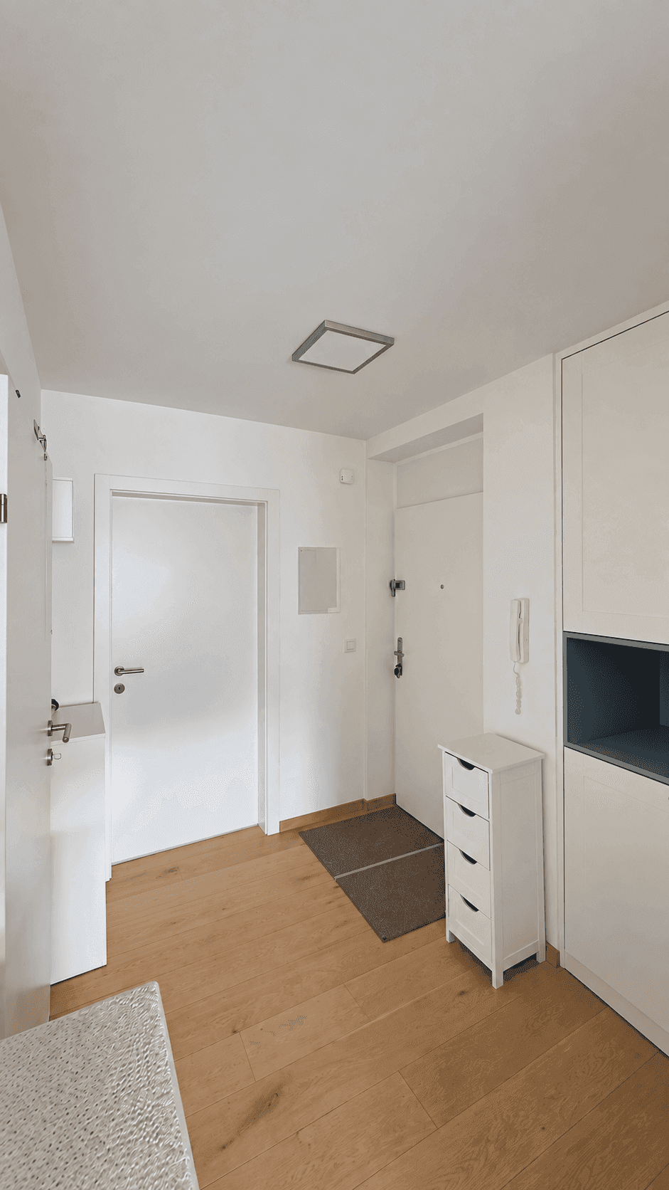 Heller Eingangsbereich mit Holzboden, weißer Garderobe und Gegensprechanlage.