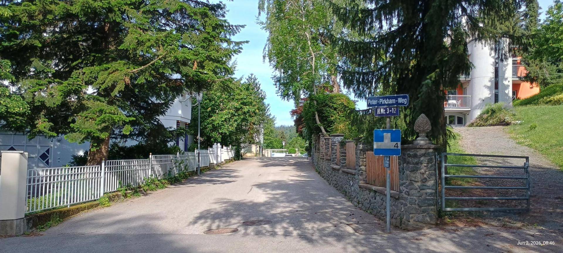 Ruhige Wohnstraße mit Bäumen und traditionellen Zäunen, die zur Immobilie führt.