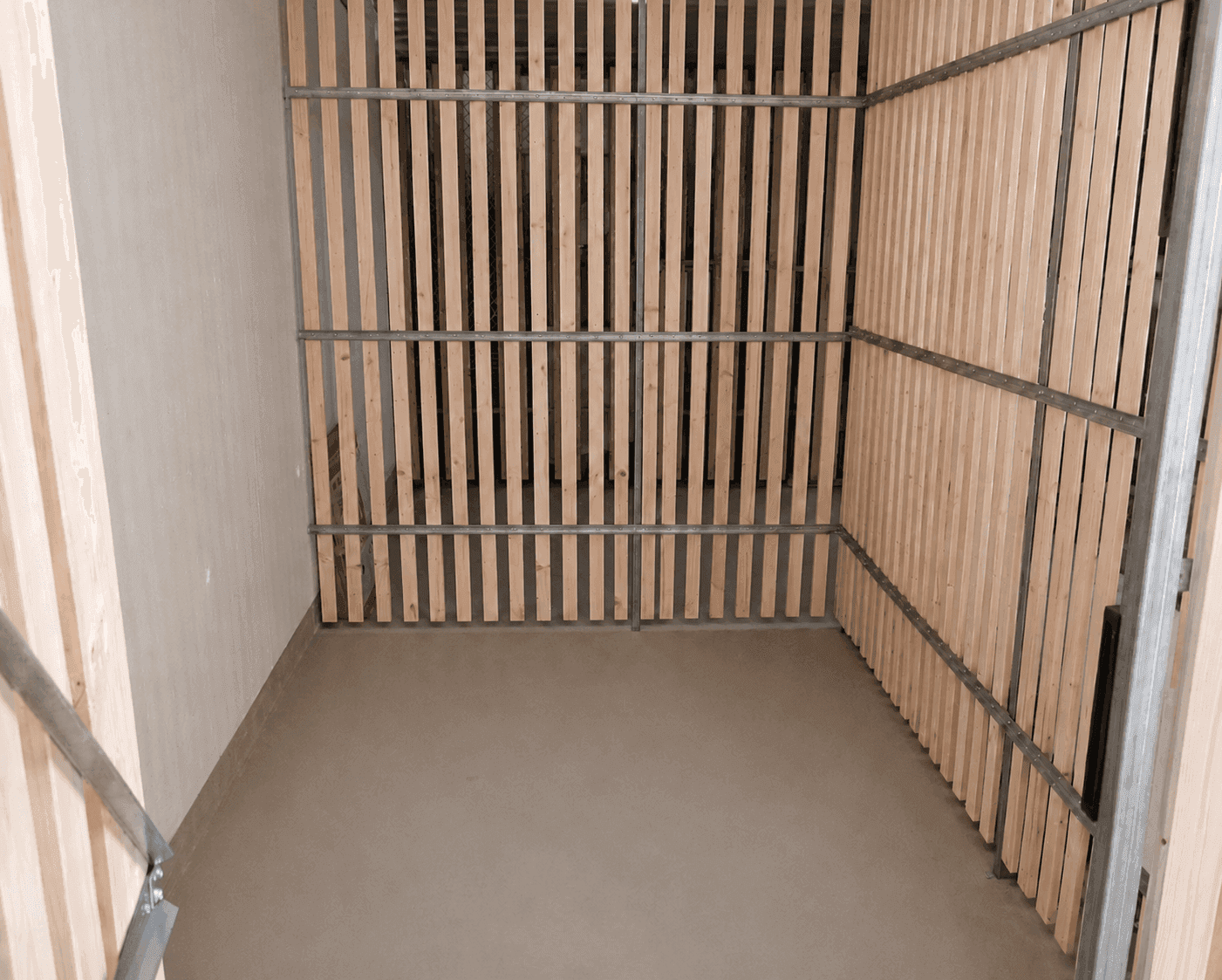 Praktischer Abstellraum mit Holzlattenwänden und robustem Betonboden für zusätzlichen Stauraum.