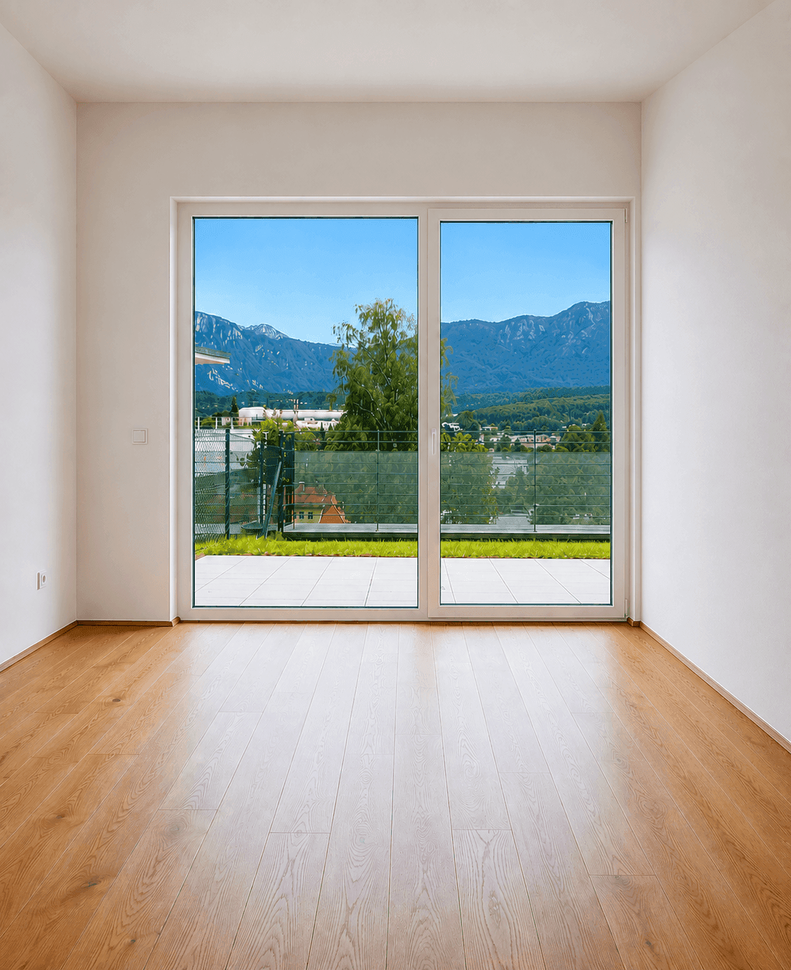 Heller Raum mit Holzboden und großer Fensterfront, die einen weiten Blick auf die Berge bietet.