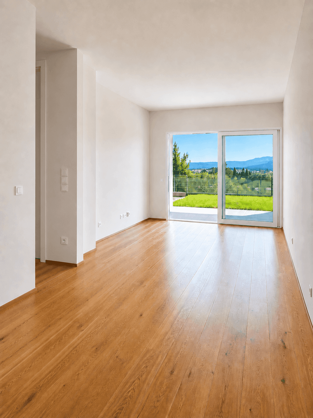 Heller Raum mit Holzboden und großer Schiebetür, die Zugang zu einer Terrasse und dem Garten bietet.