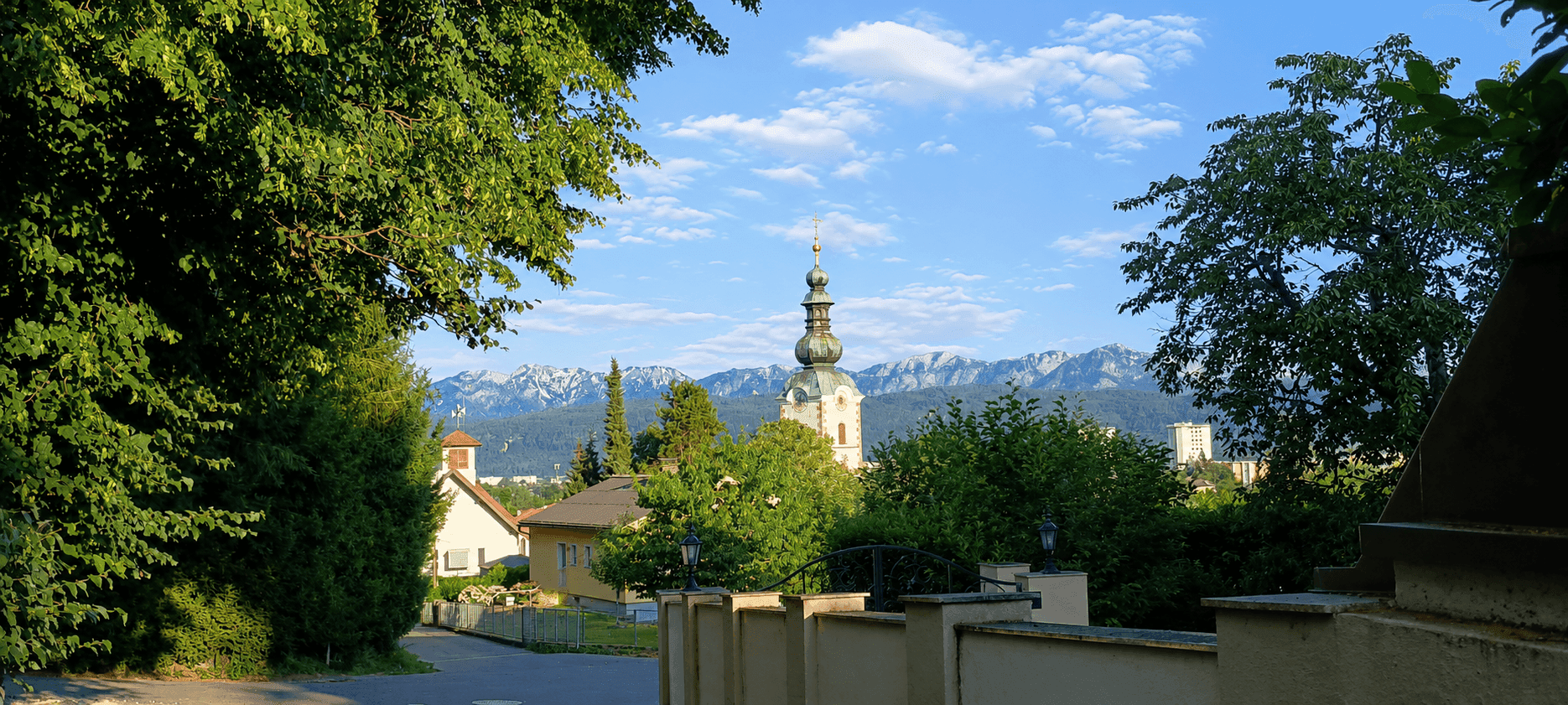Panoramablick auf einen Kirchturm und die majestätischen Berge, umrahmt von üppigem Grün.