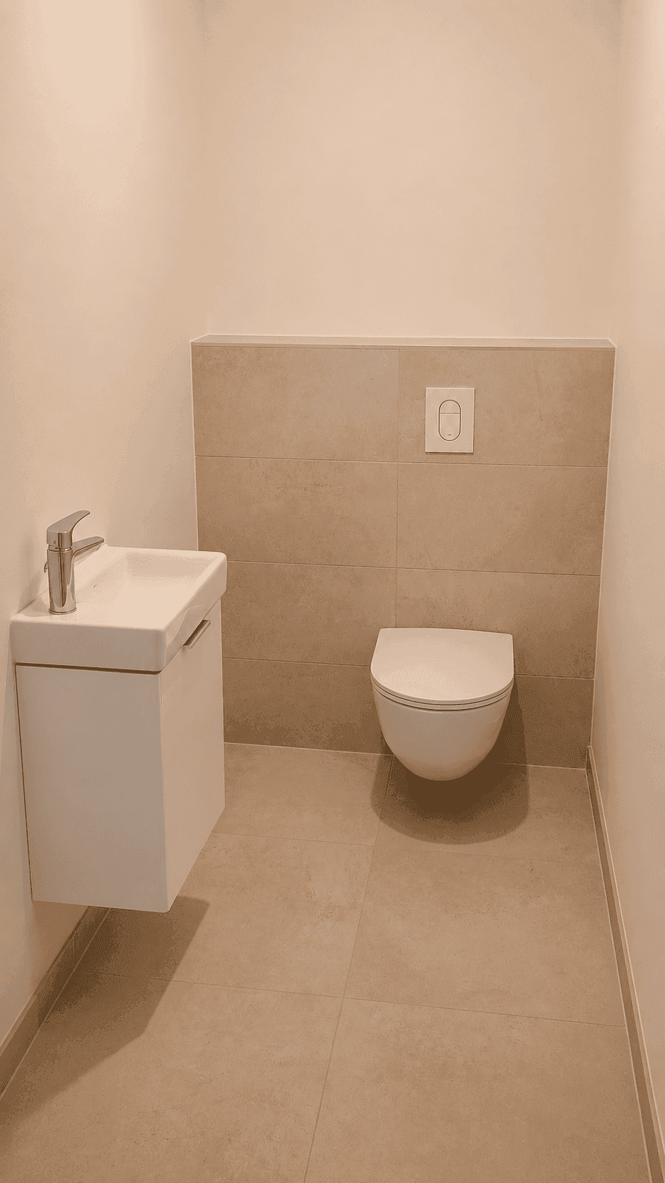 Kompaktes Gäste-WC mit wandhängender Toilette und kleinem Waschbecken, in beigen Tönen gehalten.
