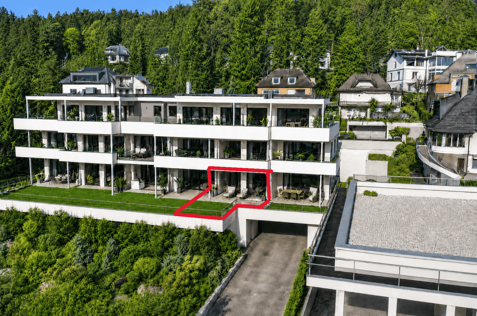 Luftaufnahme eines modernen Apartmentgebäudes mit Terrassen und Gärten, umgeben von grüner Landschaft.
