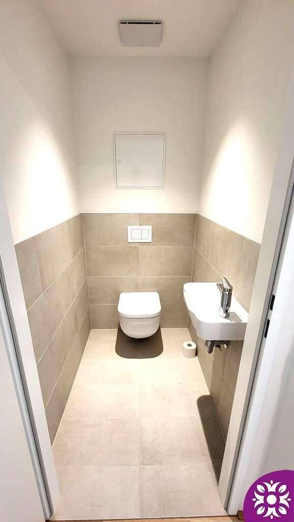 Kleines Gäste-WC mit Wand-WC, Waschbecken und halbhohen Fliesen.