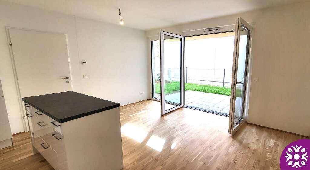 Geräumiger Wohnbereich mit Holzboden, Kochinsel und großen Glastüren zum Außenbereich.