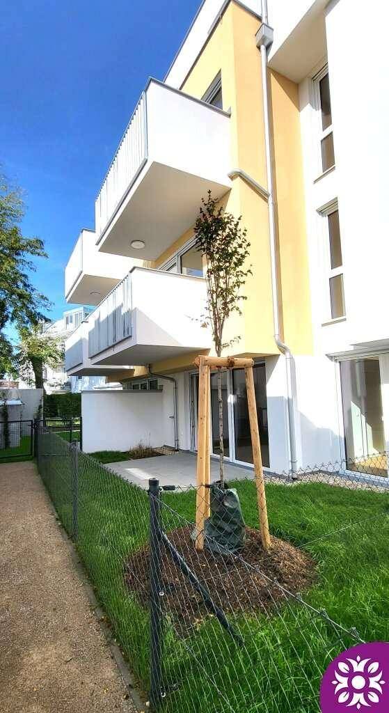 Moderne Gebäudefassade mit Balkonen und einem jungen Baum im Vorgarten.
