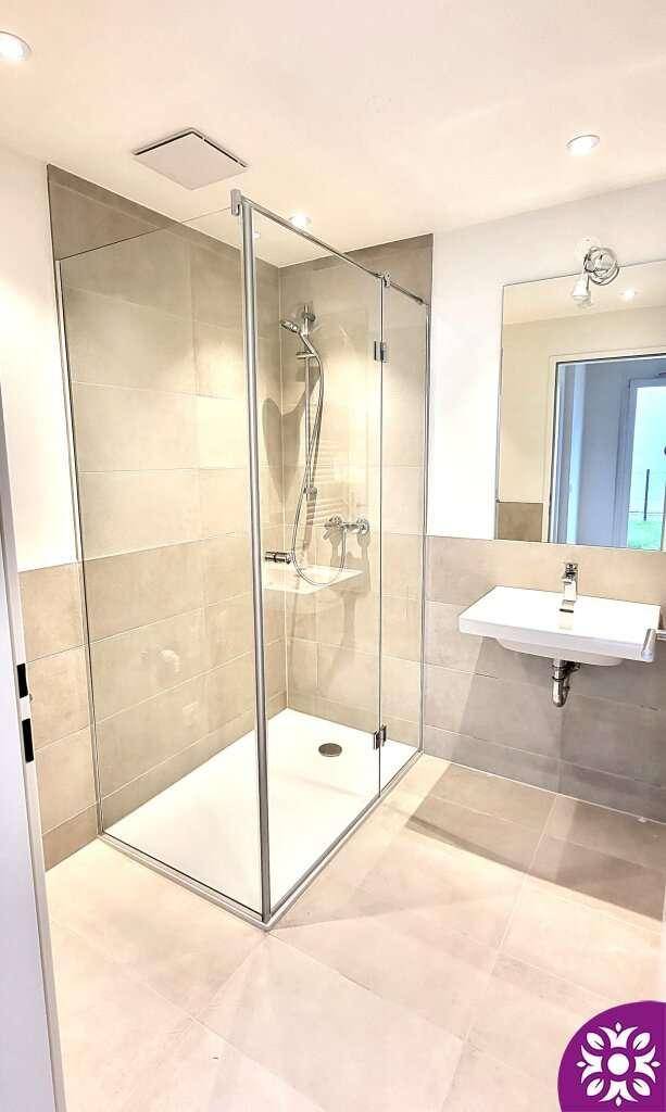 Modernes Badezimmer mit begehbarer Dusche, hellen Fliesen und einem einzelnen Waschbecken.
