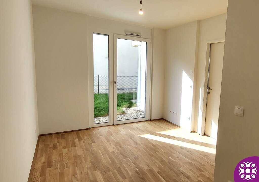 Heller Wohnraum mit Holzboden und großen Fenstern, die viel Tageslicht hereinlassen und Zugang zum Garten bieten.