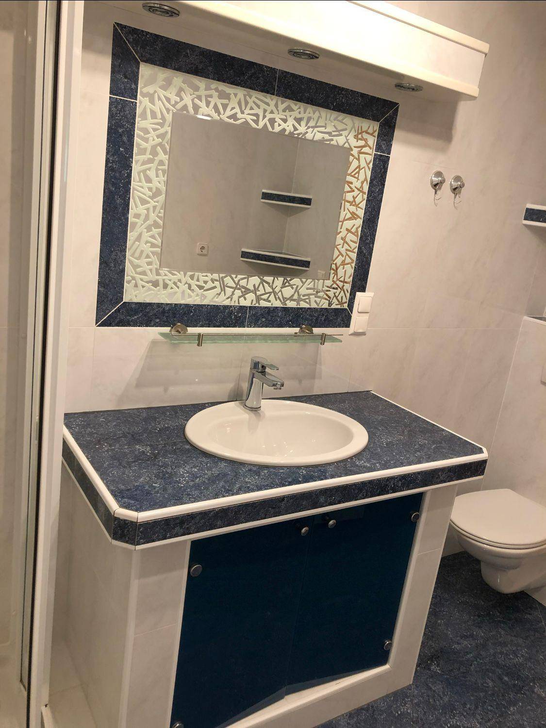 Badezimmer mit modernem Waschtisch, Spiegel und blauen Details, passend zum Gesamtbild.