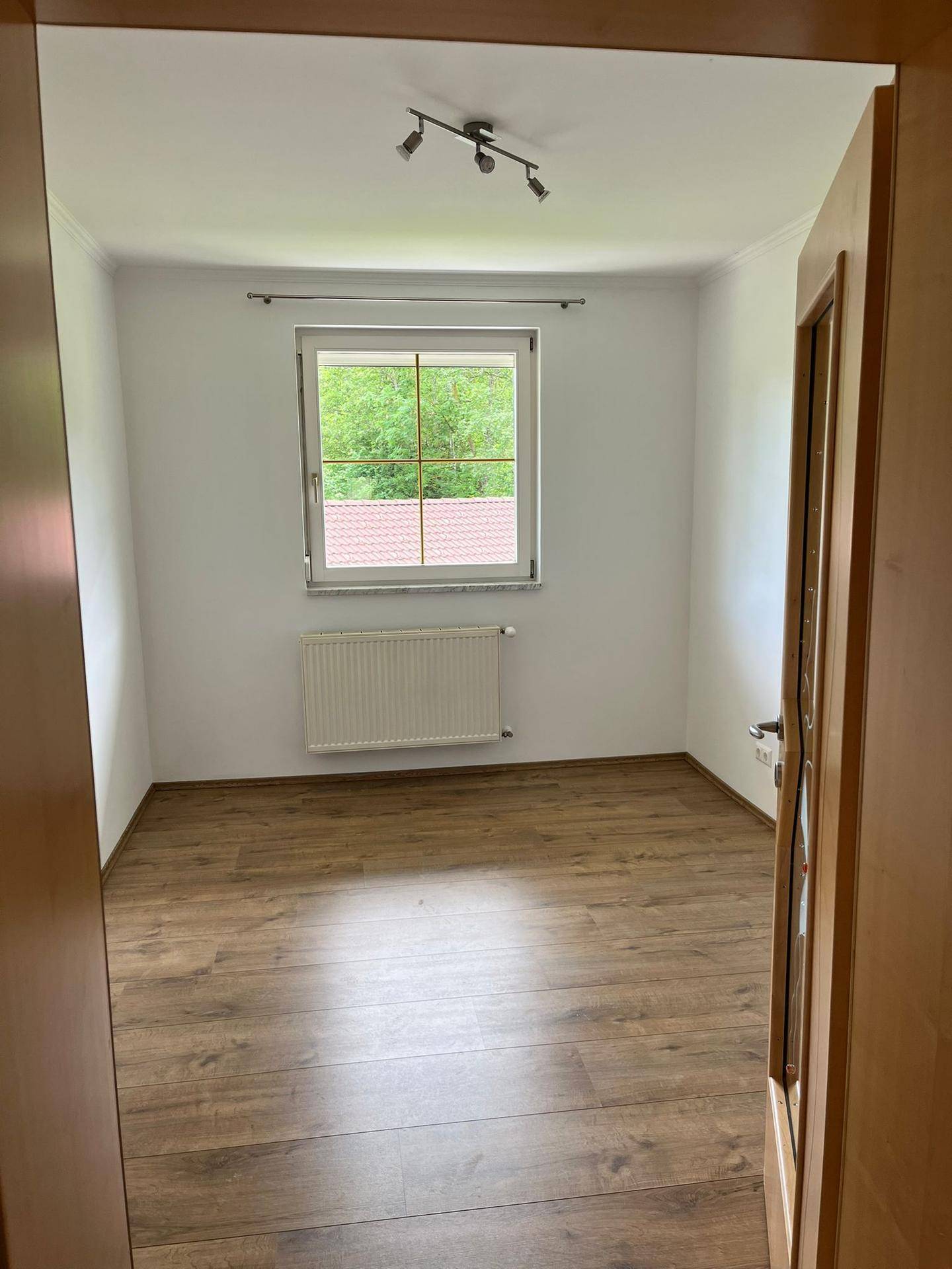Helles Schlafzimmer mit Laminatboden, großem Fenster und Blick ins Grüne.
