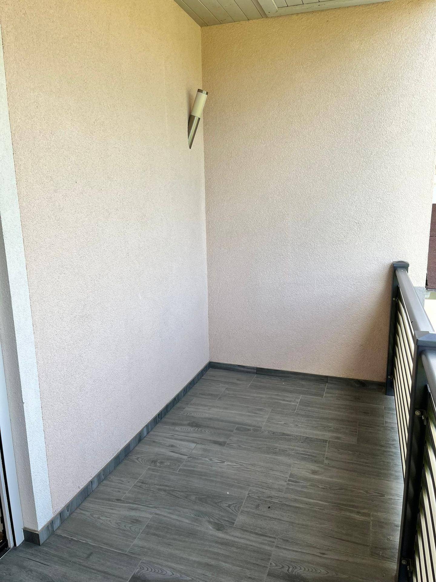 Kleiner, überdachter Balkon mit Fliesenboden und schlichtem Geländer.