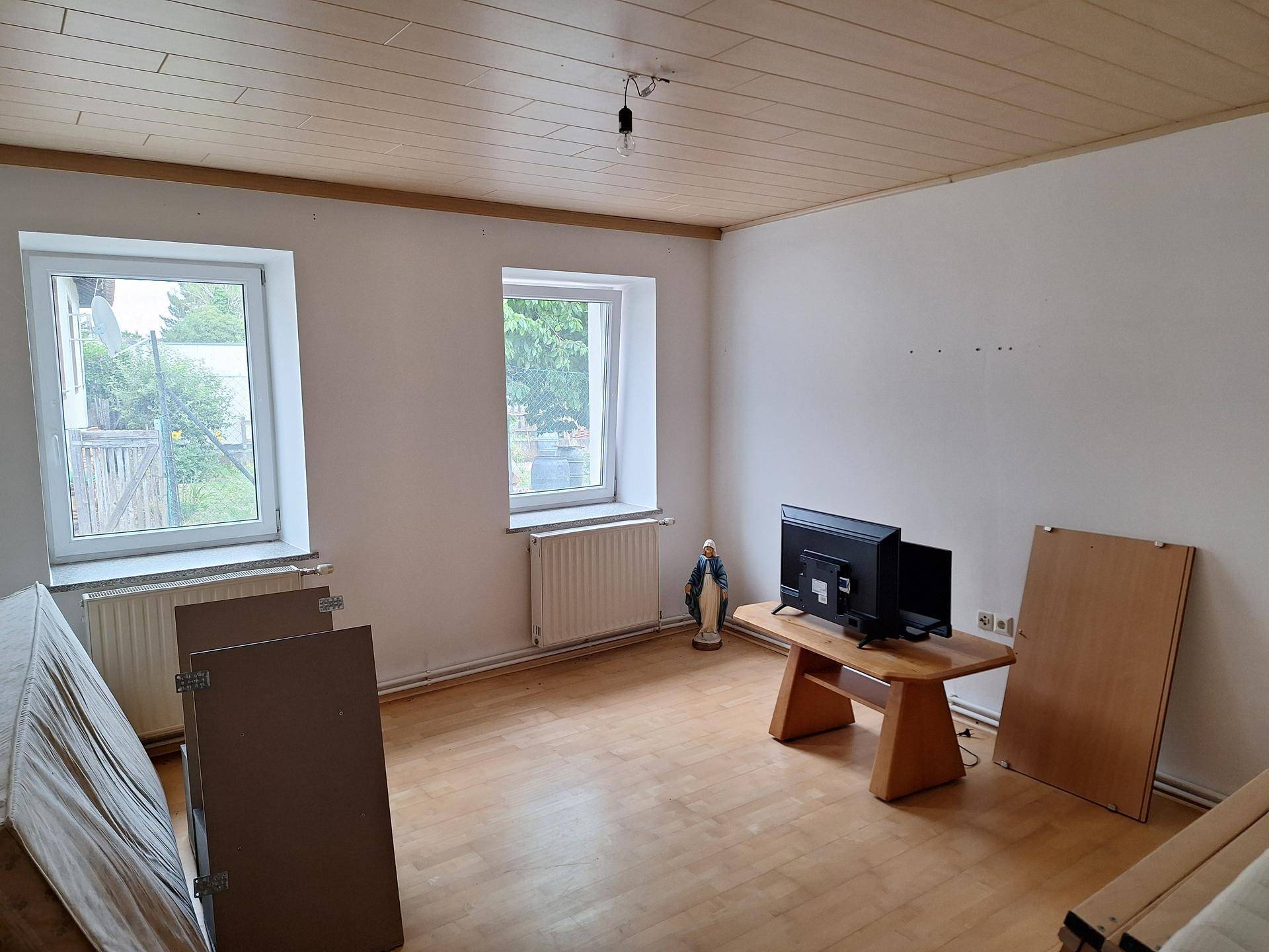 Heller Raum mit zwei Fenstern, Holzboden und Holzdecke.
