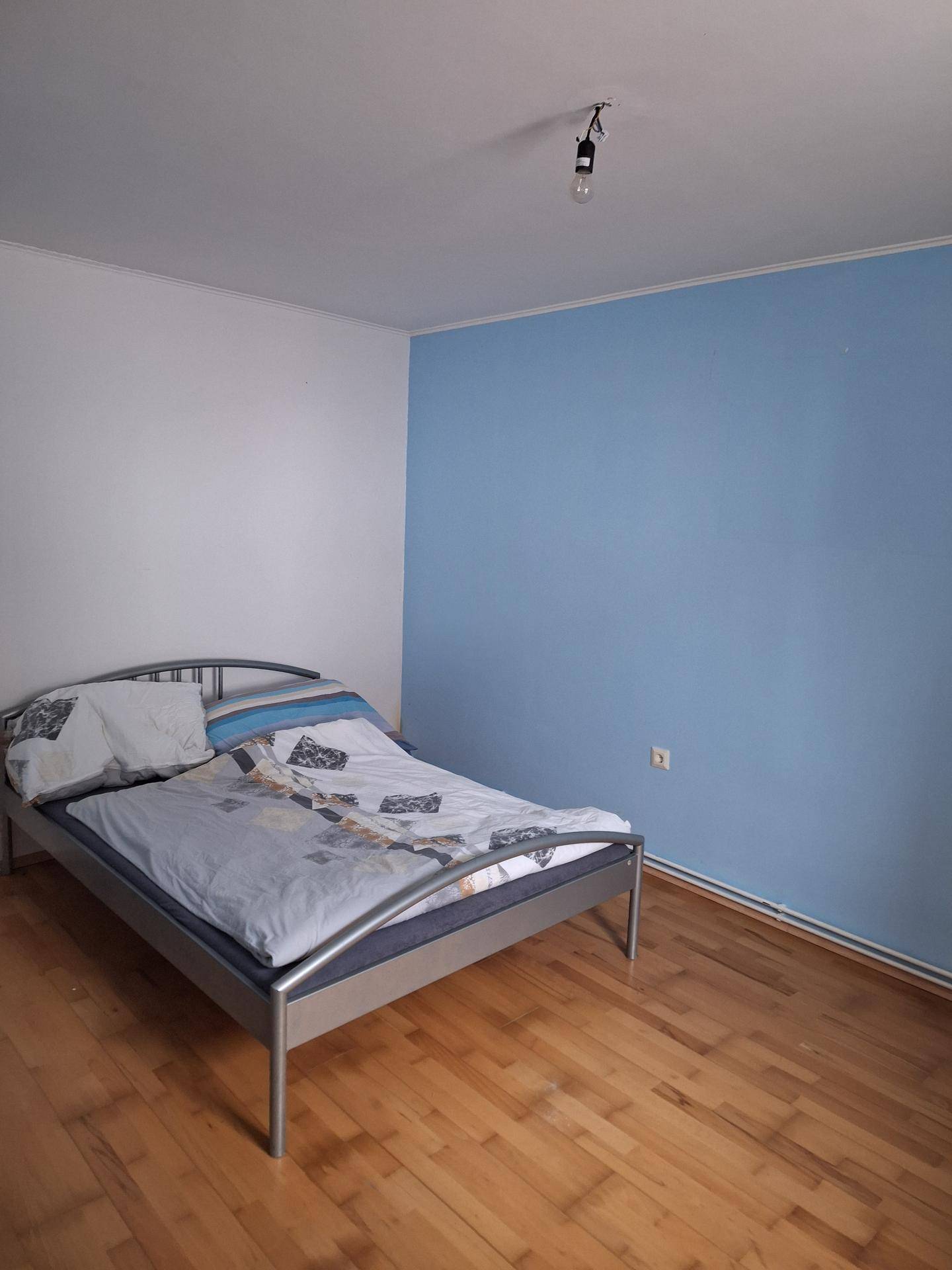 Schlafzimmer mit Holzboden und einer auffälligen blauen Akzentwand.