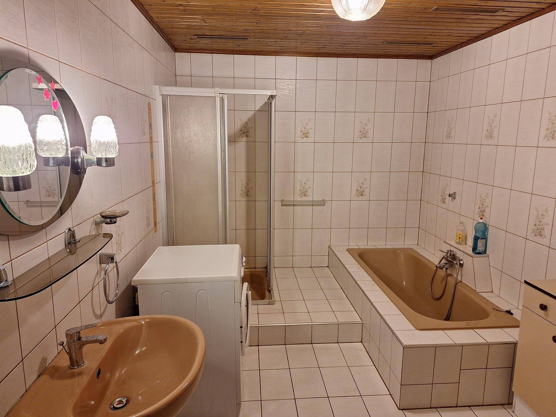 Badezimmer mit beigefarbenen Fliesen, eingebauter Badewanne und separater Dusche.