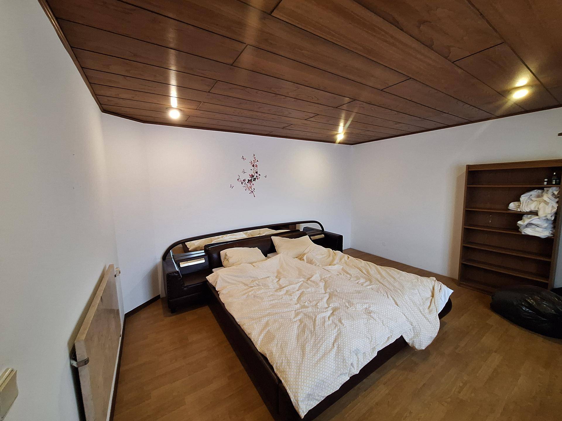 Schlafzimmer mit Holzbalkendecke, Parkettboden und einem modernen Bettgestell.