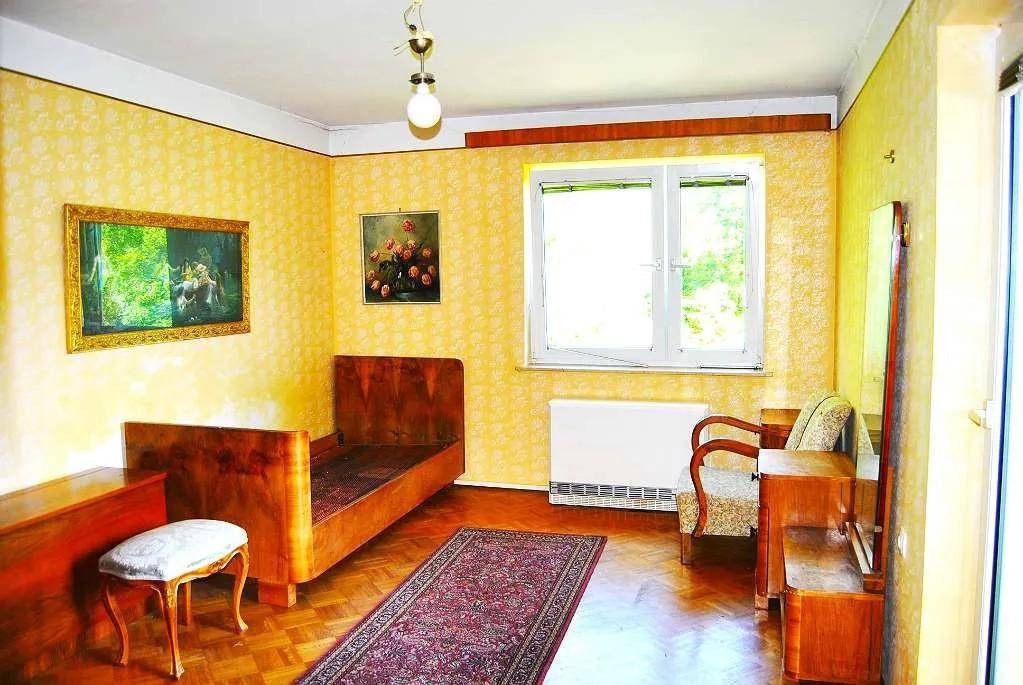 Schlafzimmer mit Einzelbett, Holzparkett und gemusterten gelben Tapeten.