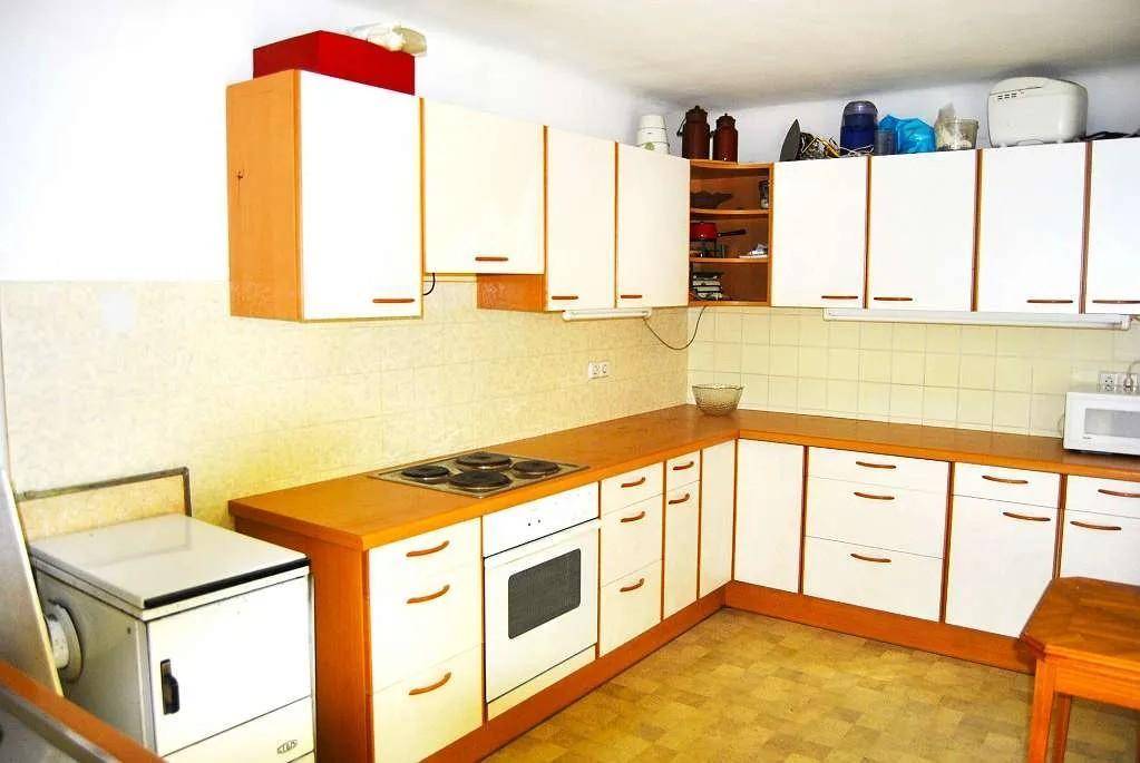 Funktionale Küche mit weißen Schränken, Holzarbeitsplatten und älteren Geräten.