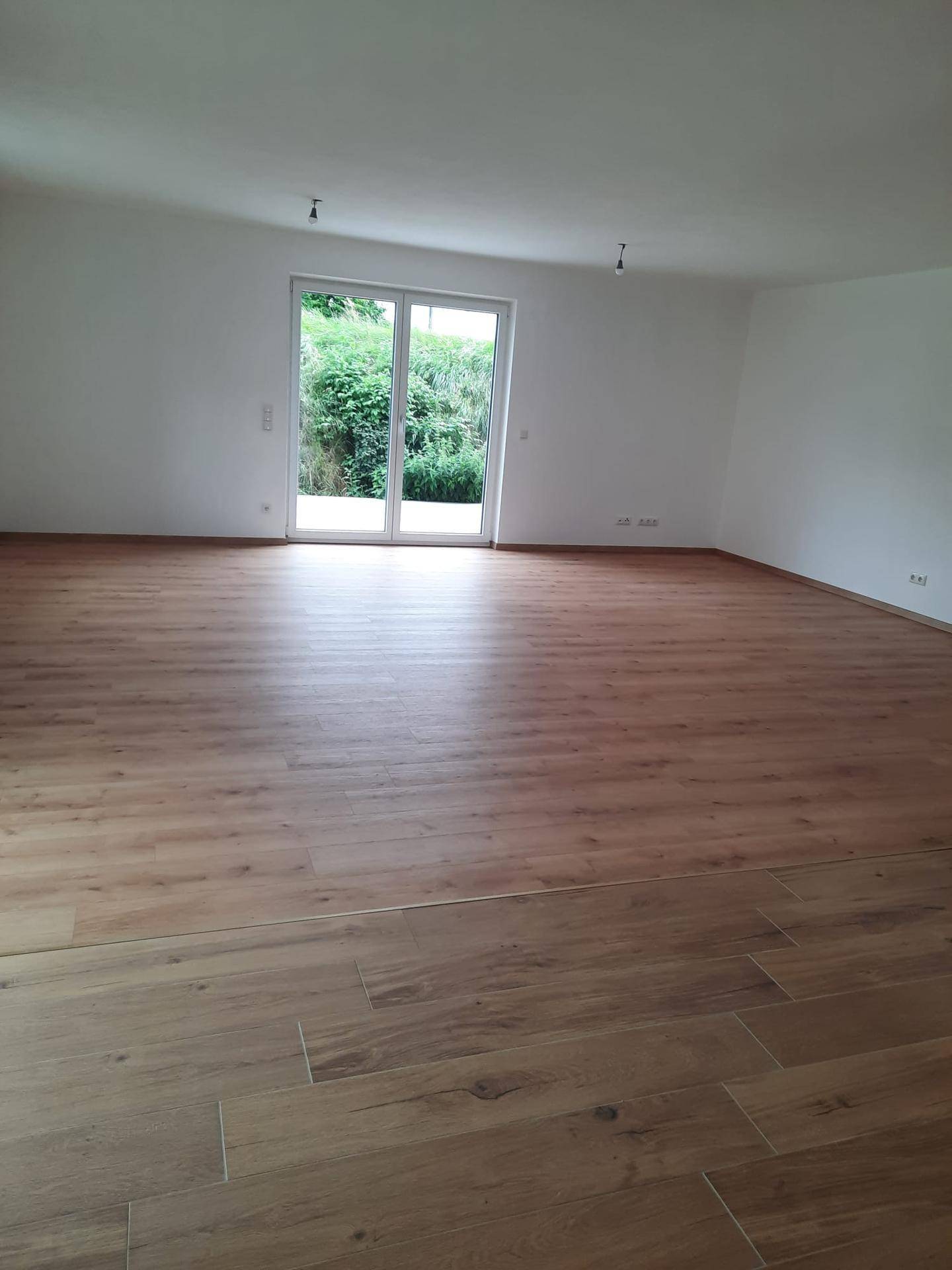 Helles, unmöbliertes Wohnzimmer mit Laminatboden und großem Zugang zum Gartenbereich.