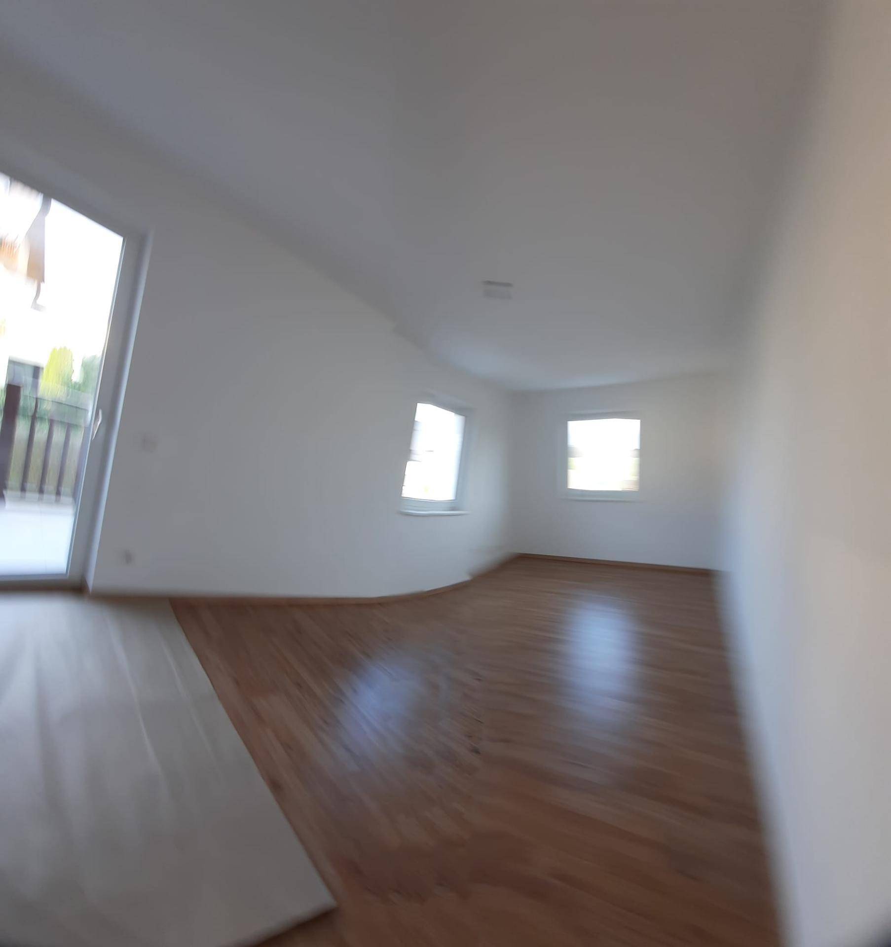 Helles Schlafzimmer mit Laminatboden, mehreren Fenstern und Zugang zu einem Balkon.