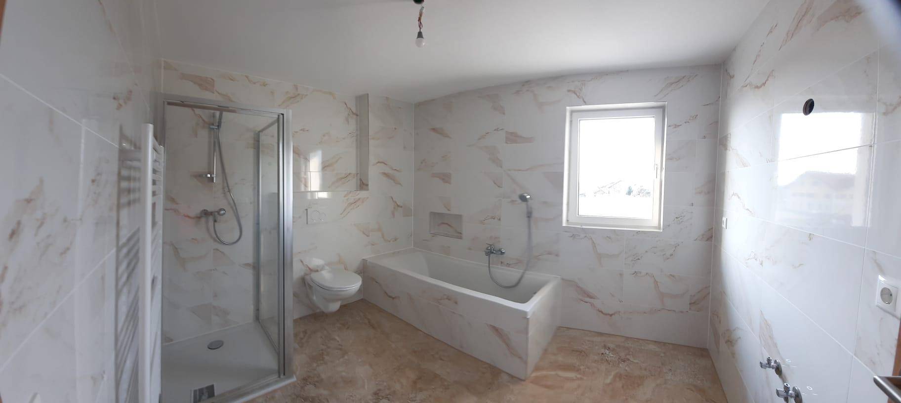 Geräumiges Badezimmer mit modernen Fliesen, Badewanne, Duschkabine und Fenster für Tageslicht.