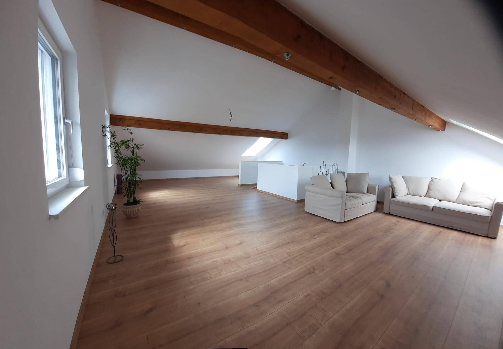 Großzügiger Dachbodenbereich mit sichtbaren Holzbalken, Dachschrägen und Laminatboden.