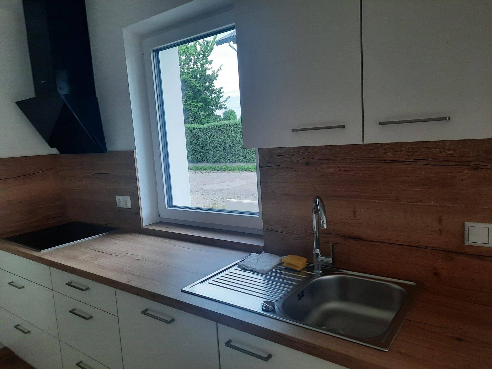 Moderne Einbauküche mit Holz-Arbeitsplatte, Spüle, Induktionskochfeld und Fensterblick ins Grüne.