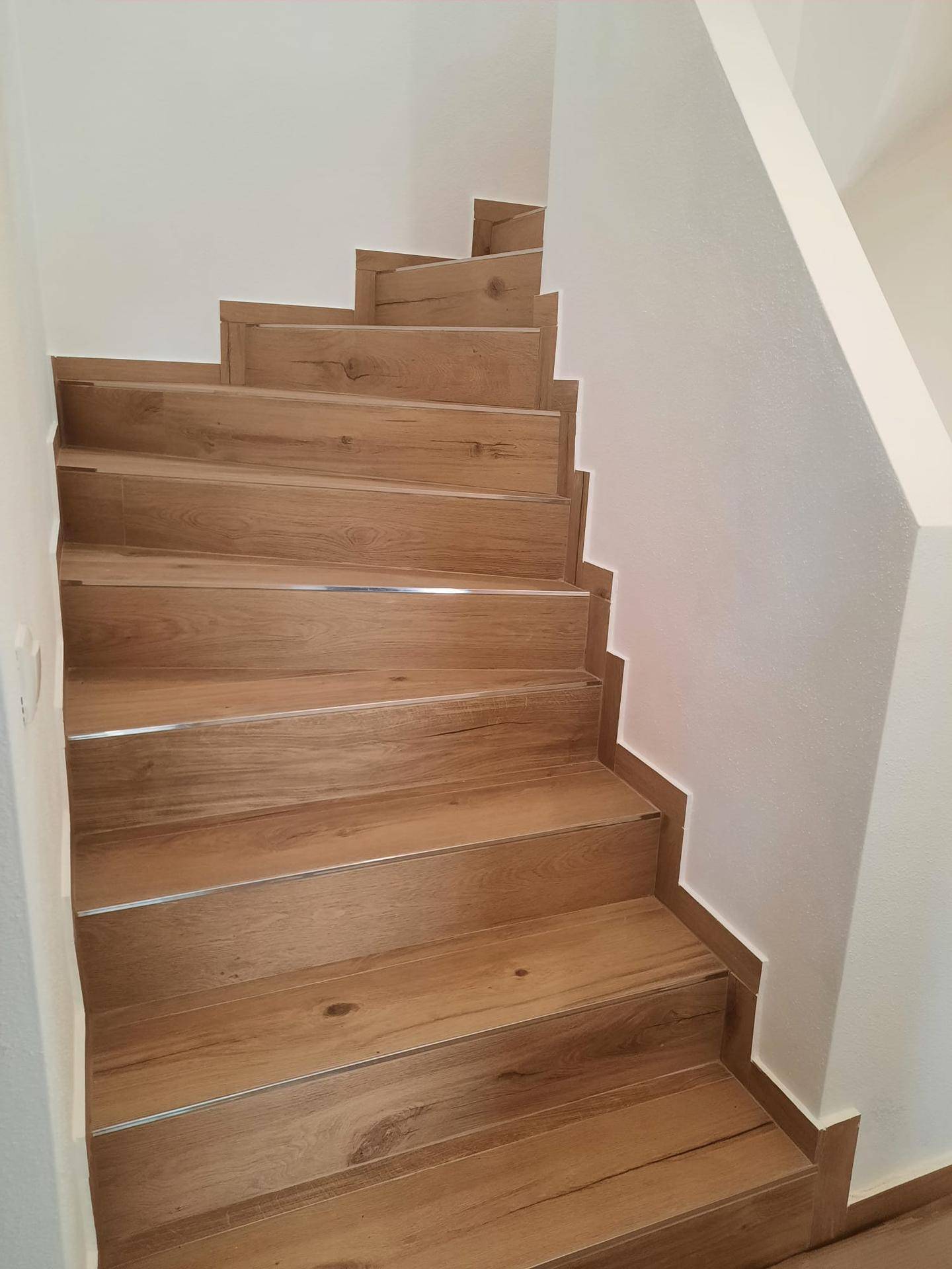 Moderne Holztreppe mit Laminatstufen und Metallleisten, die die Etagen verbindet.