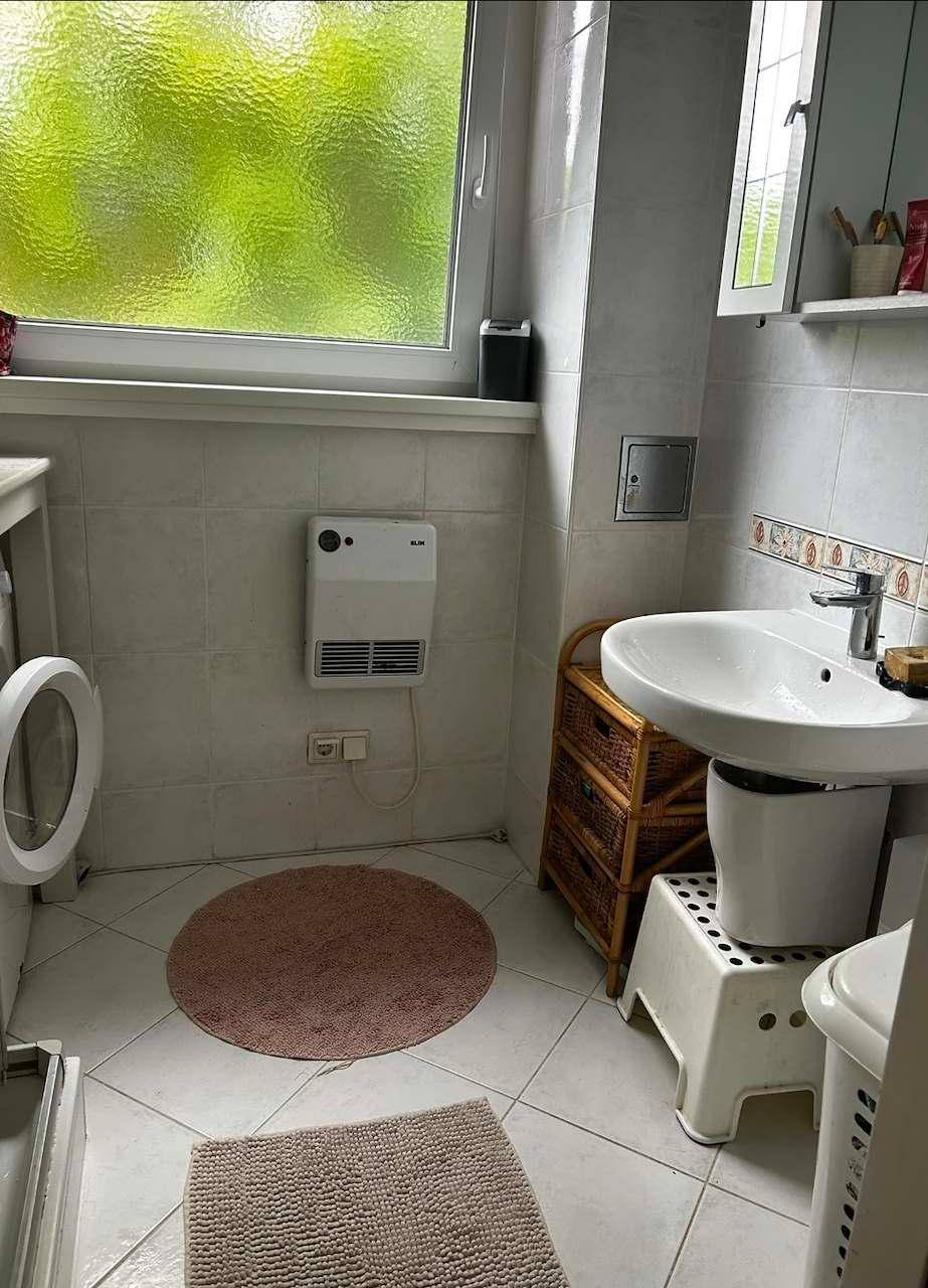 Badezimmer mit Waschbecken, Fenster und weißen Fliesen, ausgestattet mit Wandheizung.