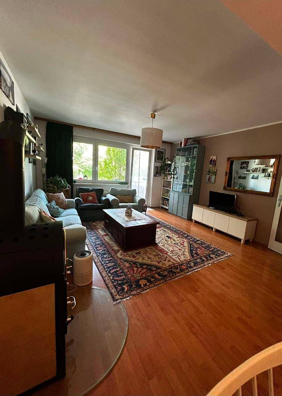 Geräumiges Wohnzimmer mit Holzboden, Kaminofen und Blick ins Grüne, hell und einladend.