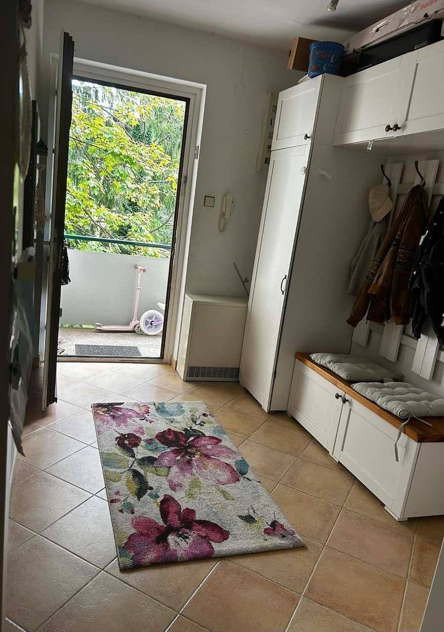 Eingangsbereich mit Fliesenboden, Garderobe und Zugang zu einem Außenbereich mit Grünblick.