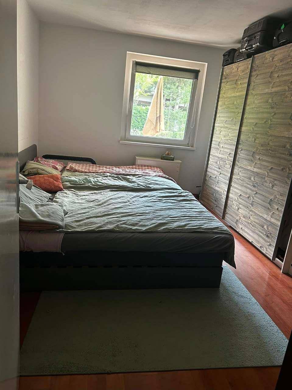 Schlafzimmer mit Doppelbett, großem Holzschrank und Fenster mit Blick ins Grüne.