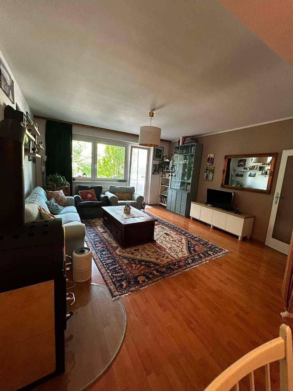 Helles Wohnzimmer mit Holzboden, Kaminofen und Zugang zum Außenbereich, gemütlich eingerichtet.