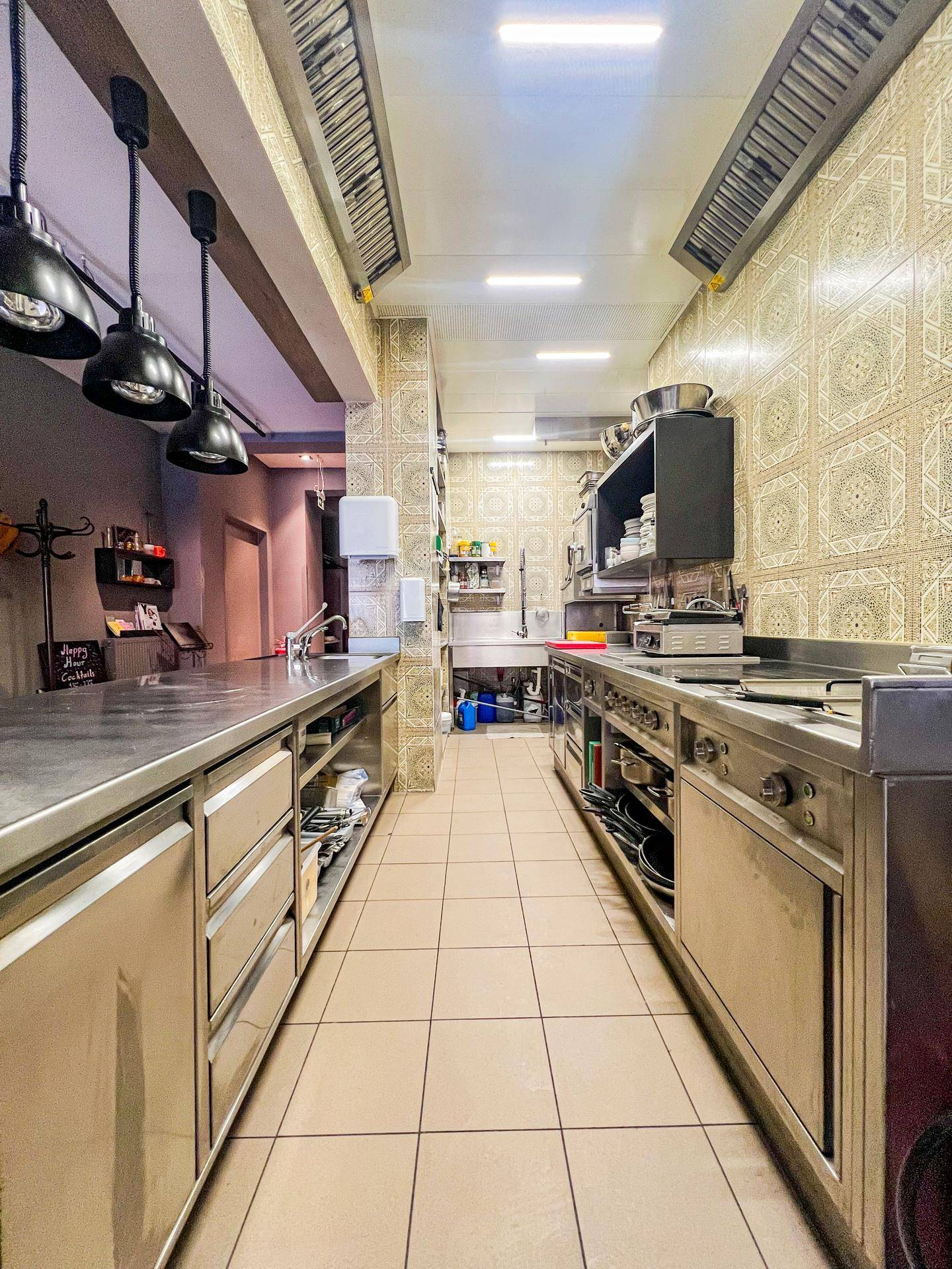 Professionelle Großküche mit Edelstahlmöbeln, Arbeitsflächen und Fliesen an den Wänden und auf dem Boden.