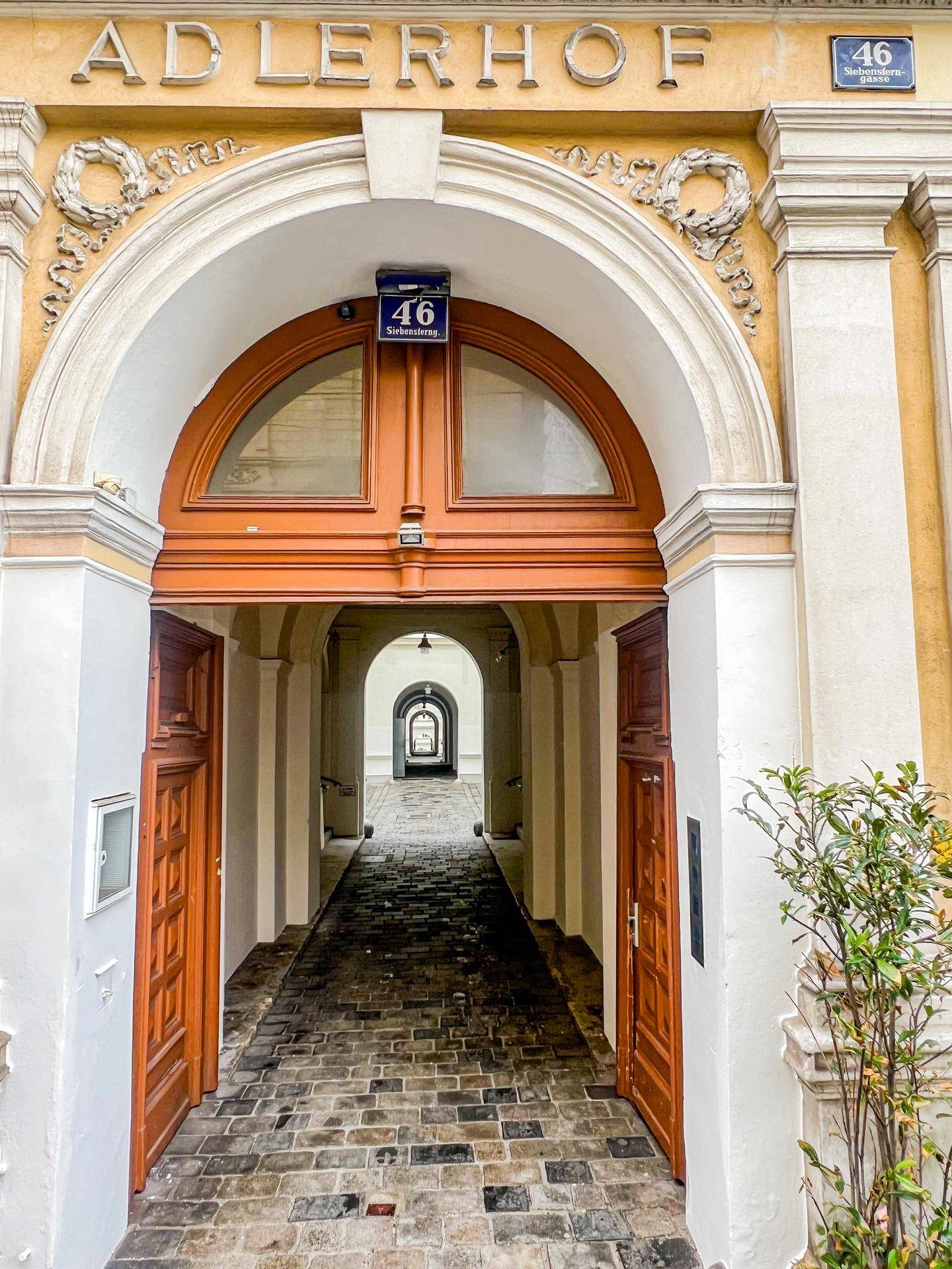 Historischer Gebäudeeingang mit einem großen Bogen, Holztüren und einem gepflasterten Durchgang.