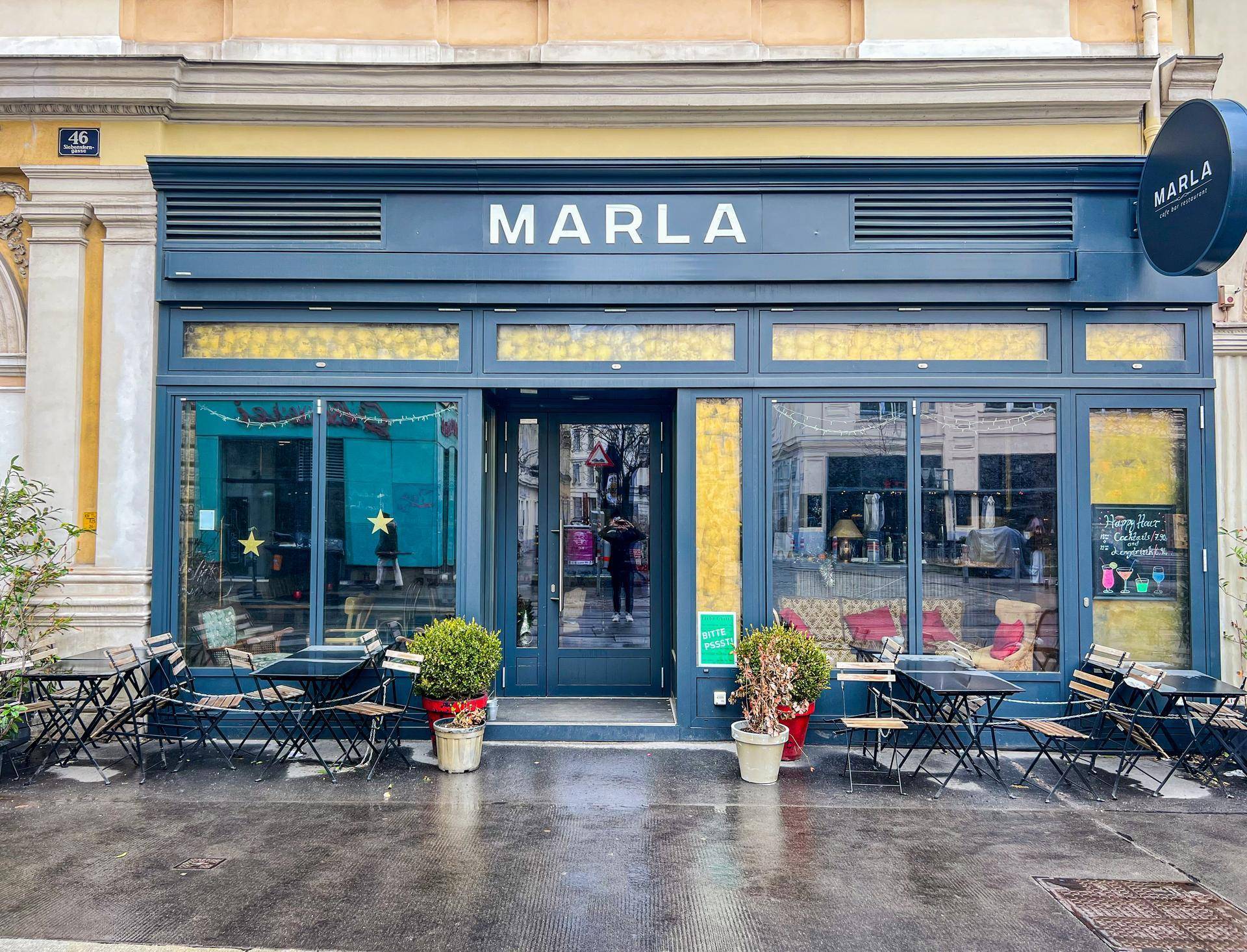 Attraktive Ladenfront mit blauer Fassade, großen Fenstern und Außensitzgelegenheiten auf dem Bürgersteig.