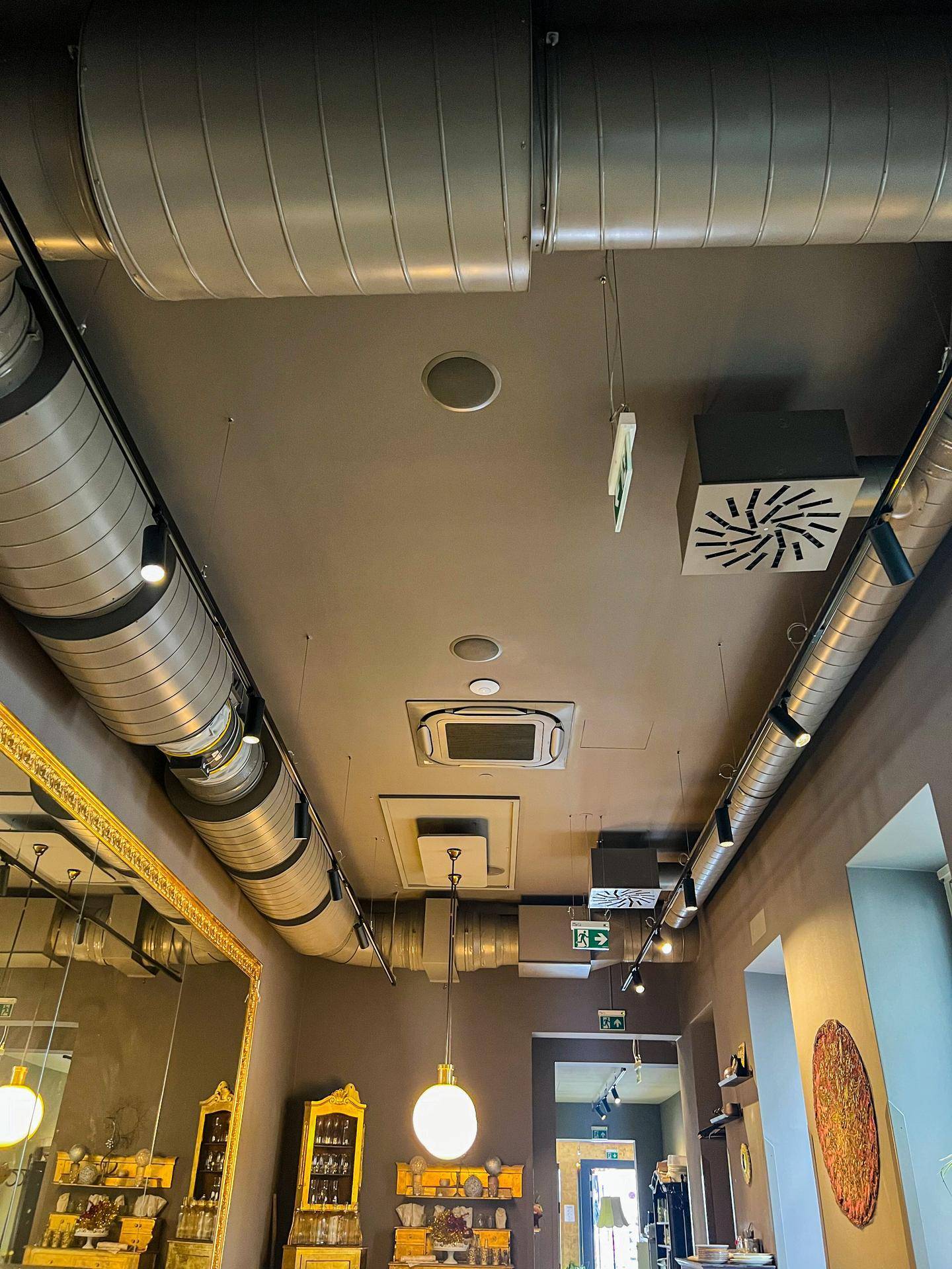 Deckenansicht eines Gastraums mit sichtbaren Lüftungsrohren, Klimaanlage und modernen Beleuchtungsschienen.
