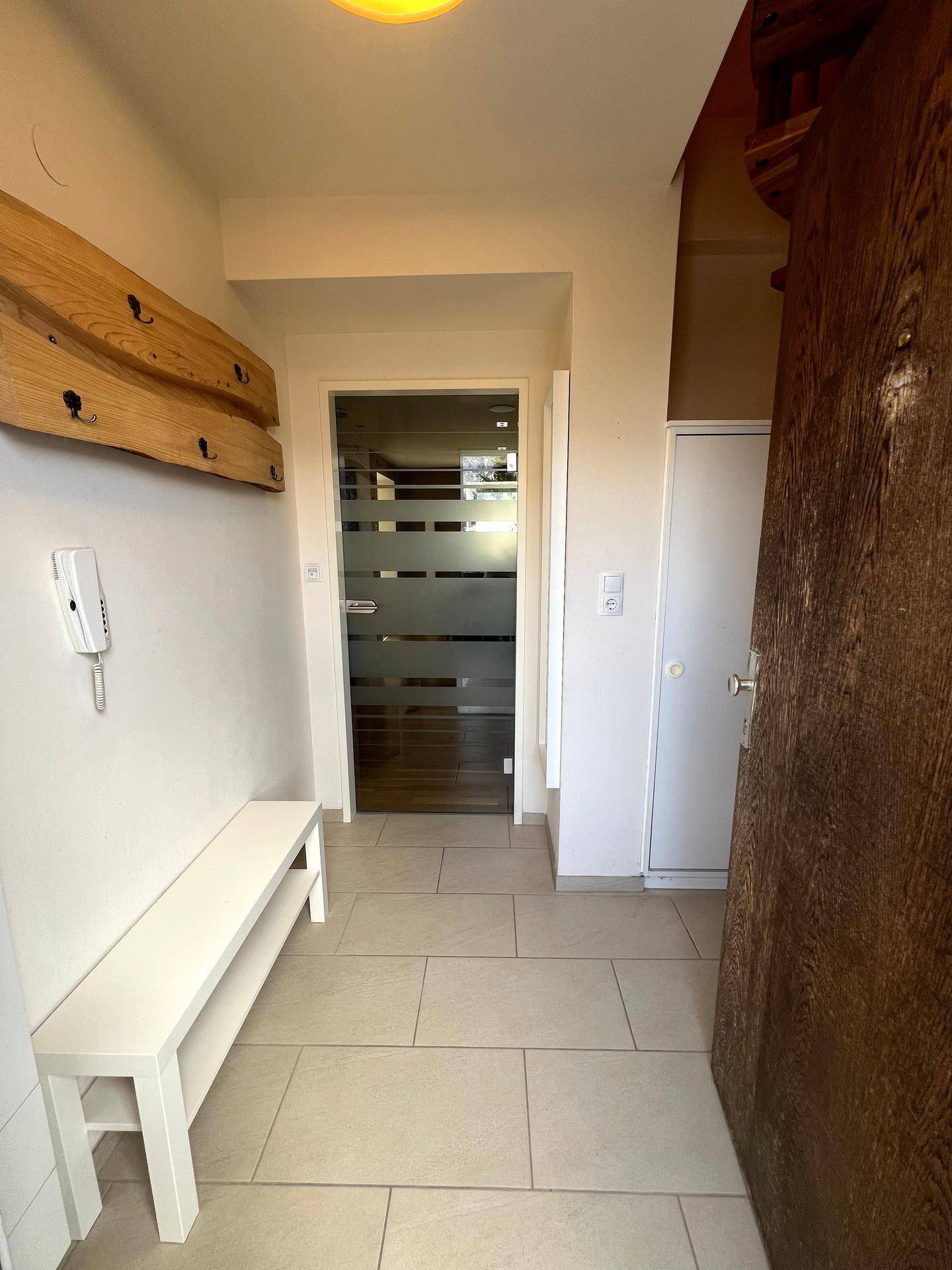 Heller Eingangsbereich mit Fliesenboden, Sitzbank und Garderobe.
