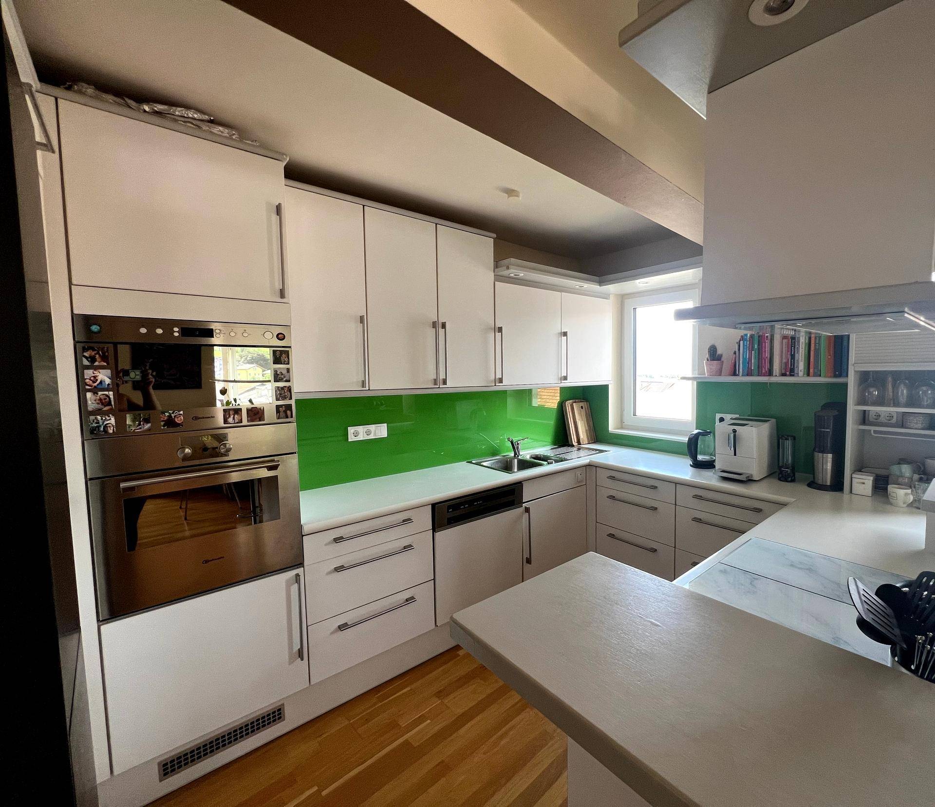 Moderne Einbauküche mit weißen Schränken, grüner Rückwand und integrierten Geräten.