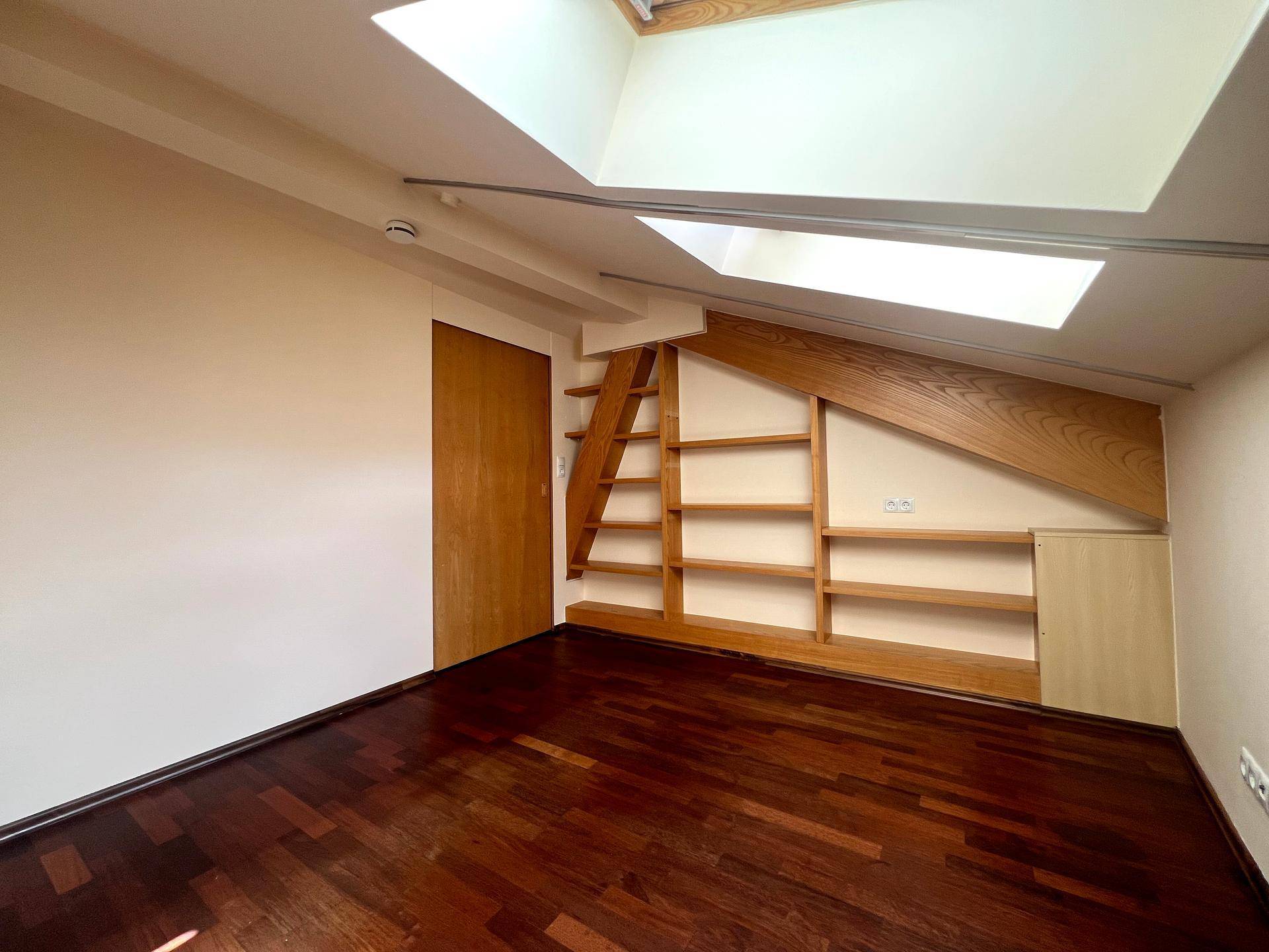 Dachzimmer mit Holzboden, Einbauregalen und Dachfenstern für natürliches Licht.