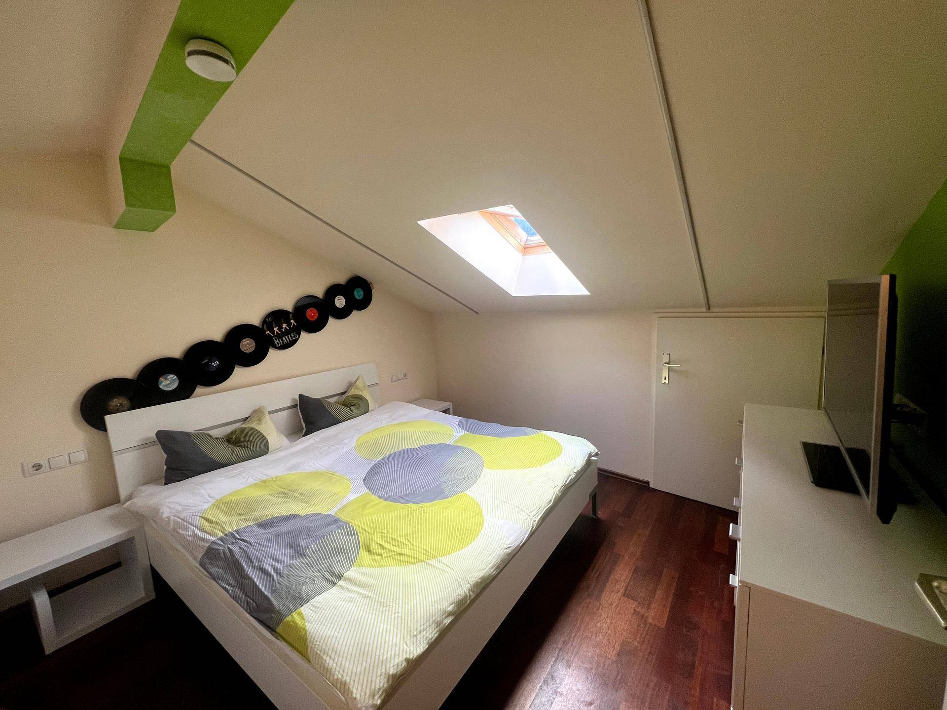 Schlafzimmer im Dachgeschoss mit Holzboden, Dachfenster und farbigen Akzenten.