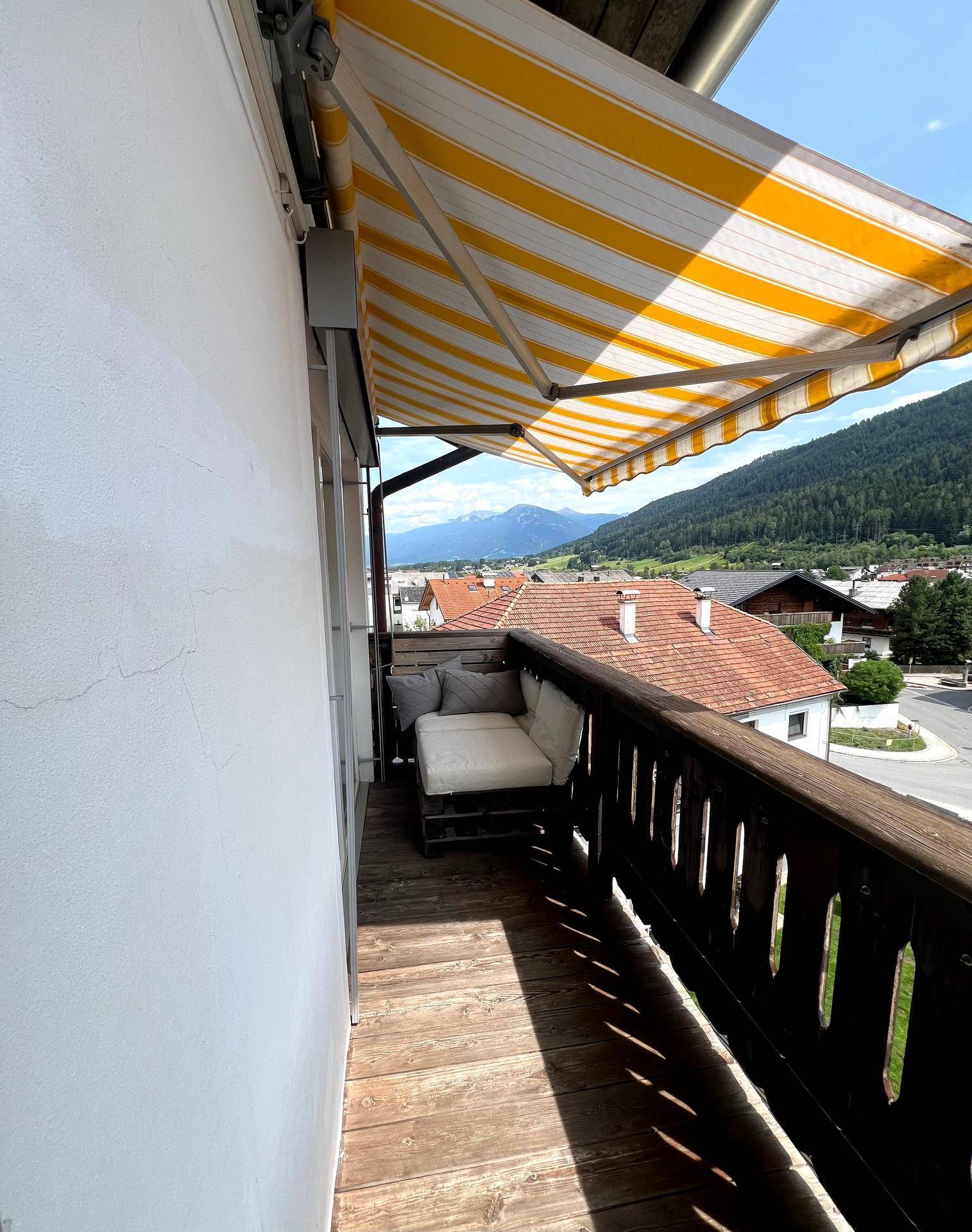 Langer Balkon mit Holzboden, Markise und Panoramablick auf die Alpenlandschaft.