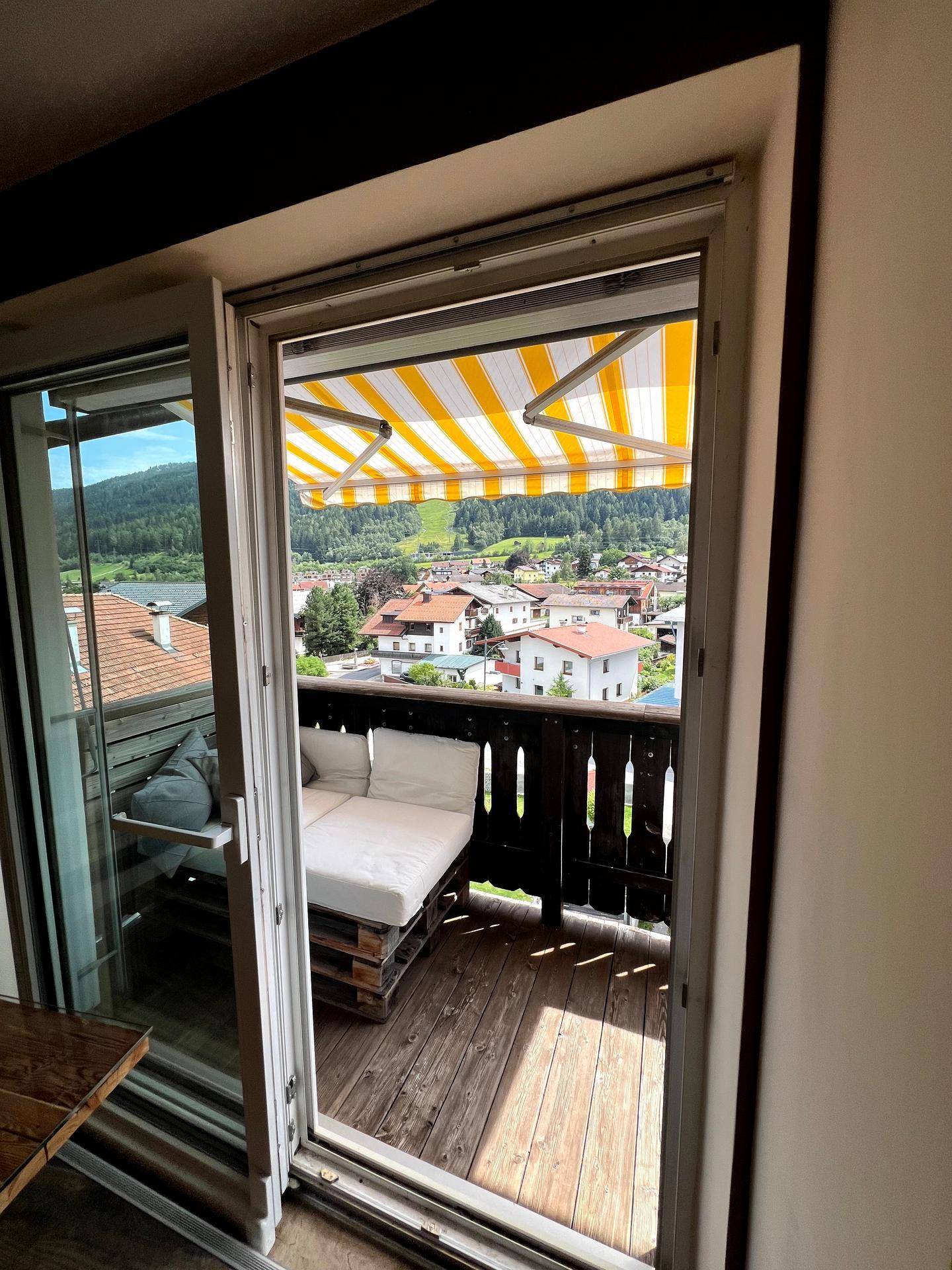 Balkon mit Markise, Sitzgelegenheiten und weitem Blick über die Dächer und Berge.