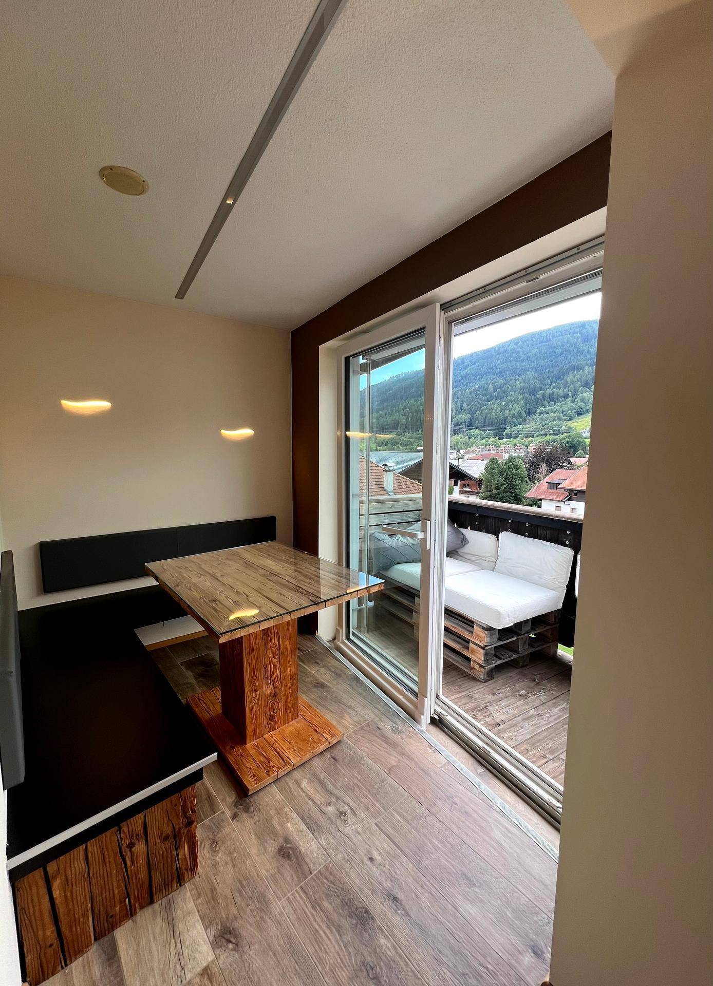 Essbereich mit Holztisch und Sitzbank, direktem Zugang zum Balkon und Bergblick.