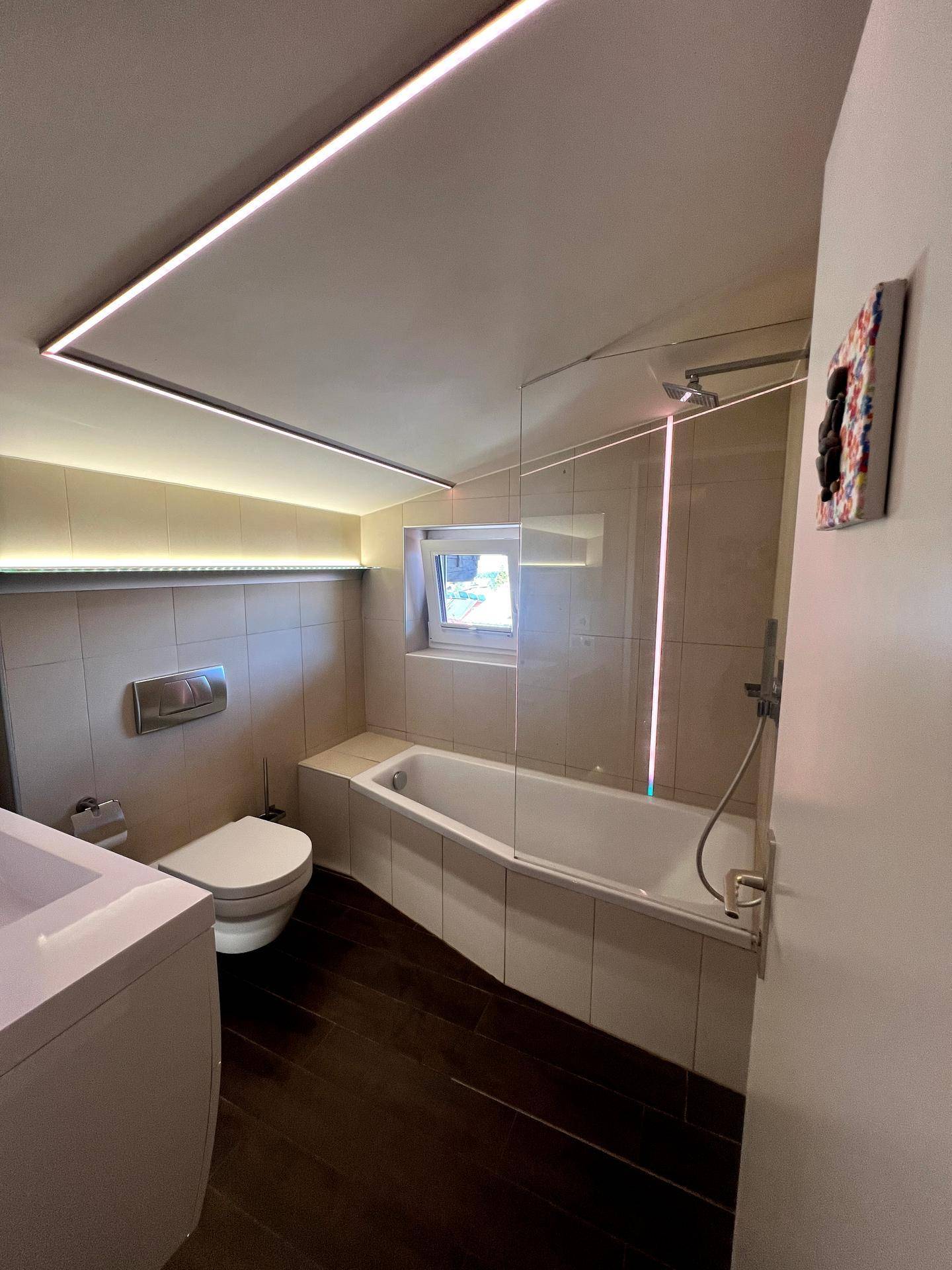 Helles Badezimmer mit Badewanne, WC, Fliesenboden und Fenster.