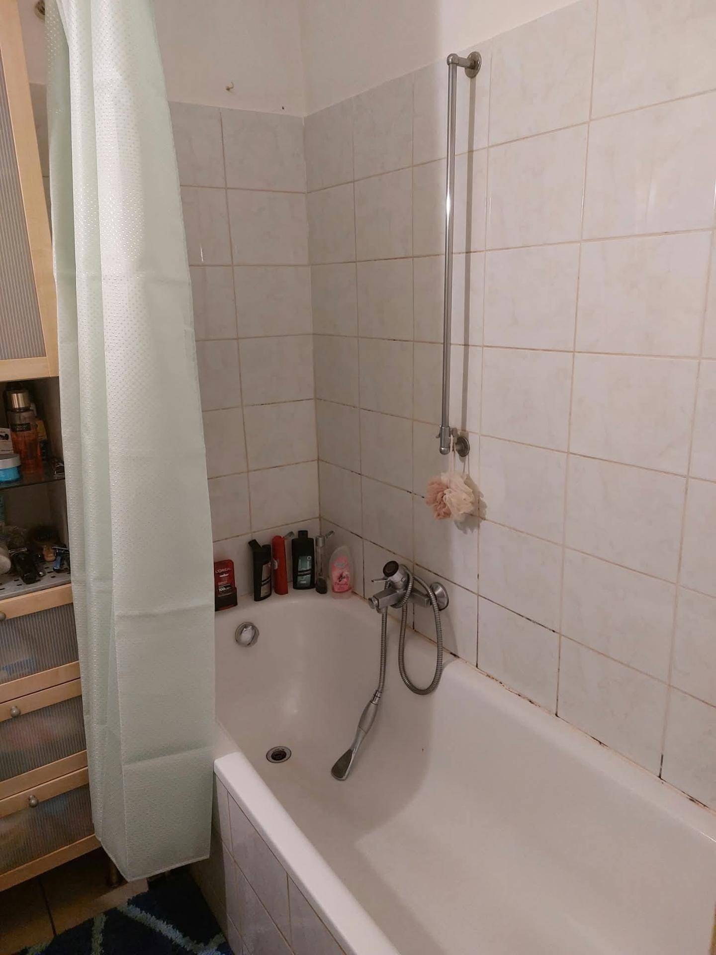 Badezimmer mit Badewanne, Duschvorhang und weißen Wandfliesen in Standardausführung.