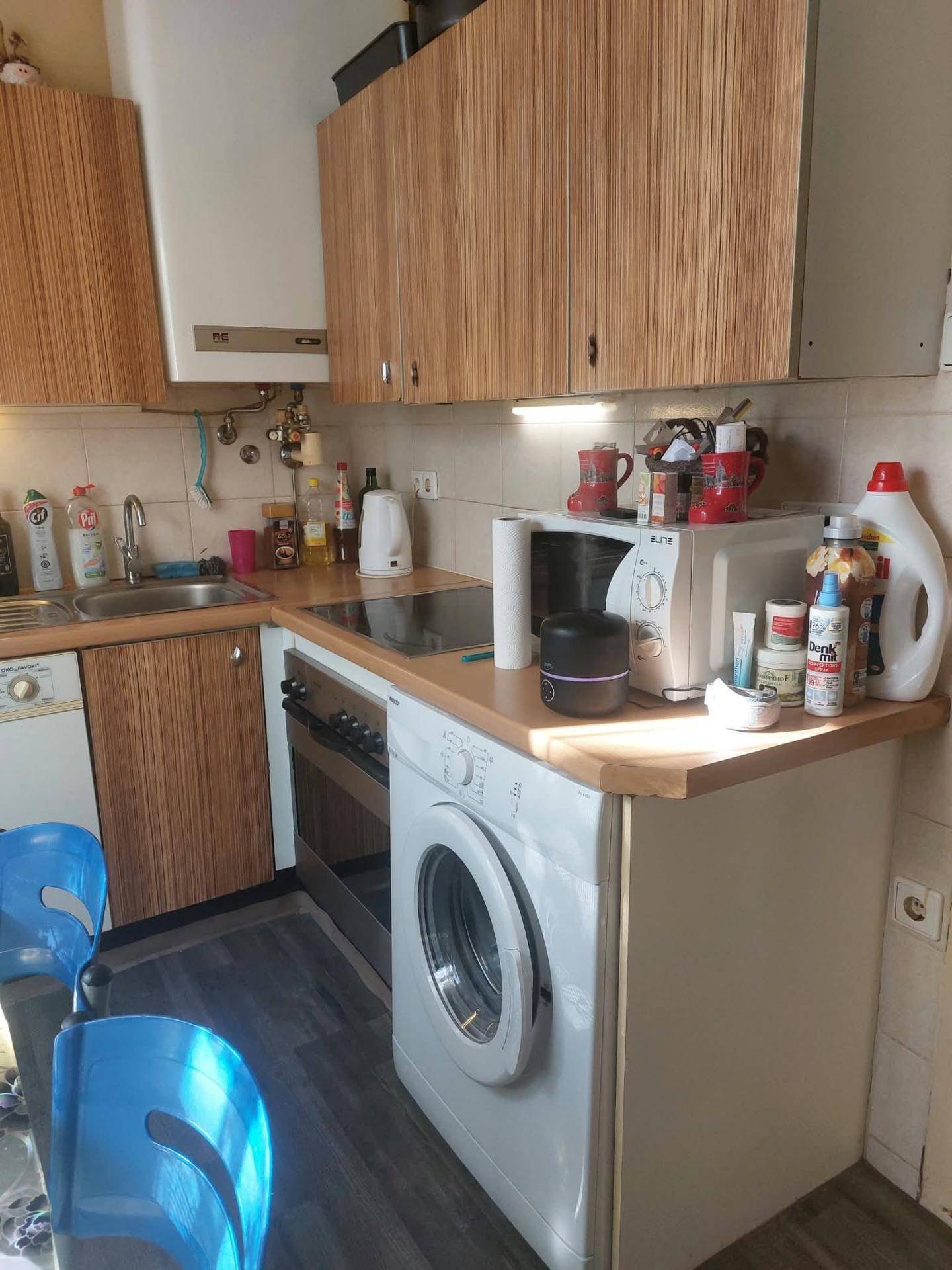 Funktionale Küche mit Holzschränken, integriertem Backofen, Kochfeld und Waschmaschine.